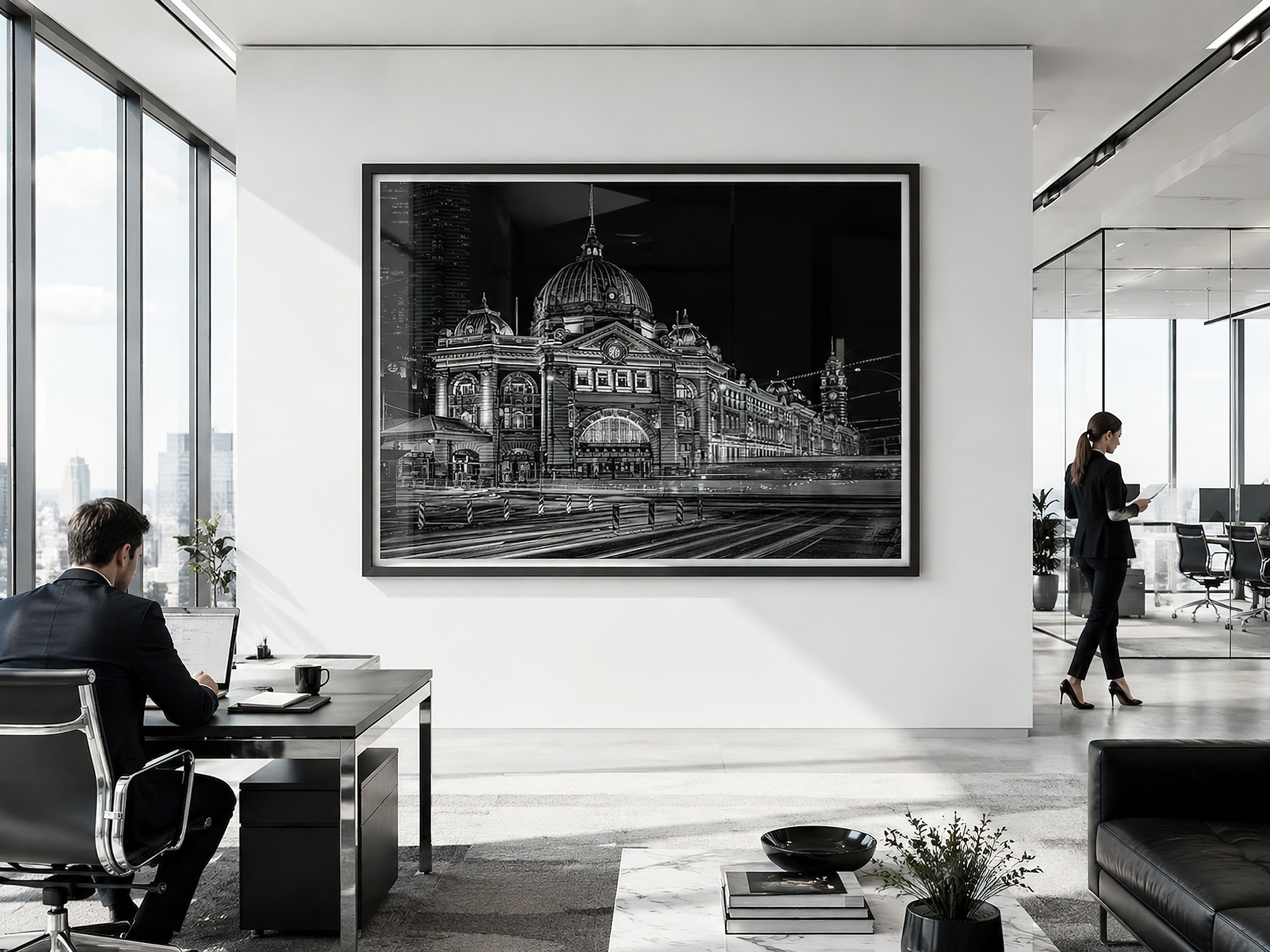 Framed black-and-white Flinders Street Station photograph with illuminated domes, historic architecture and light trails in a bright monochrome corporate office with two professionals working, by Nick Psomiadis at NIKART Studio and Gallery