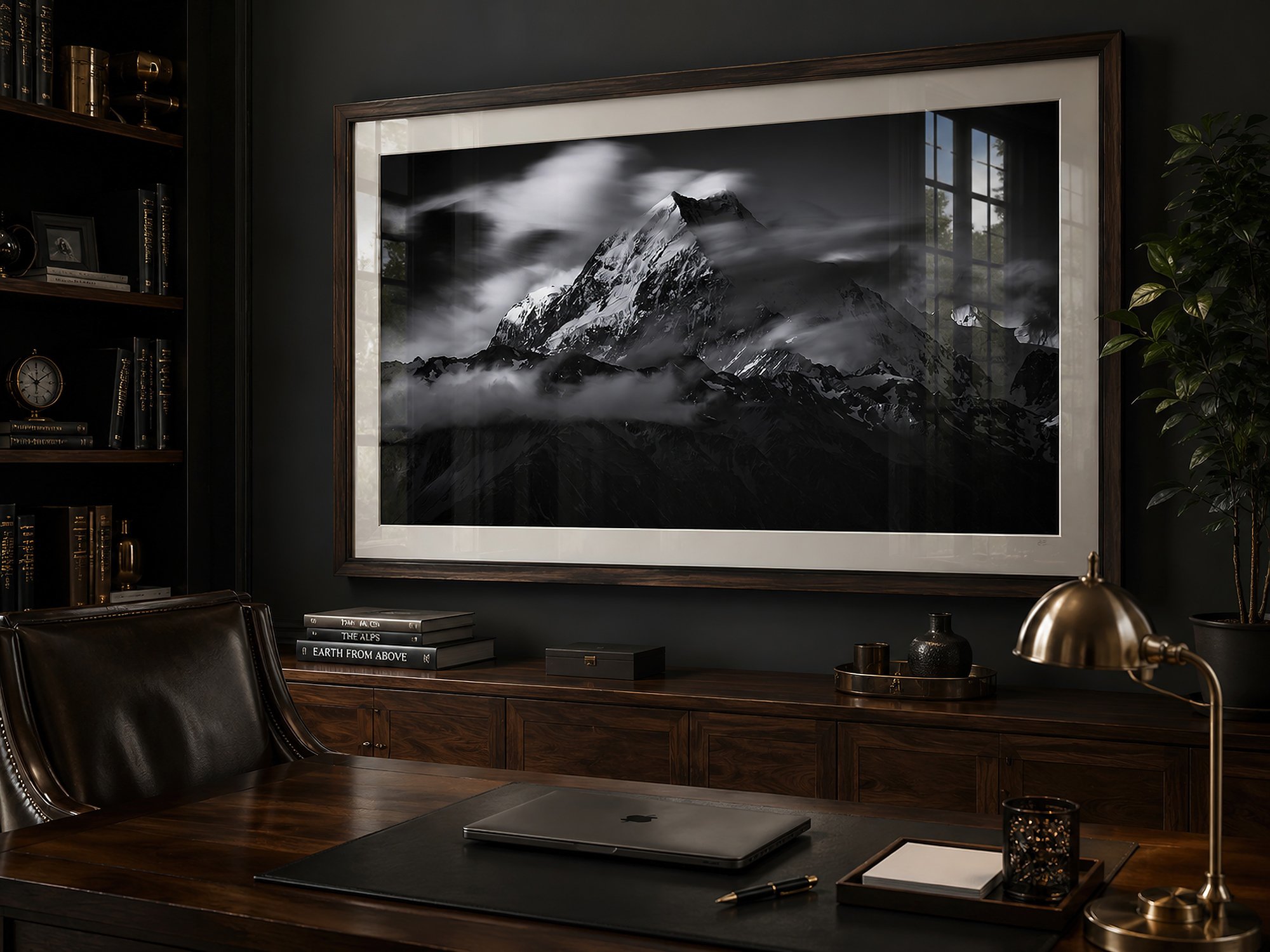 Large framed black-and-white mountain photograph in a masculine dark timber study with desk, shelving, moody lighting and realistic glass reflections by Nick Psomiadis at NIKART Studio and Gallery