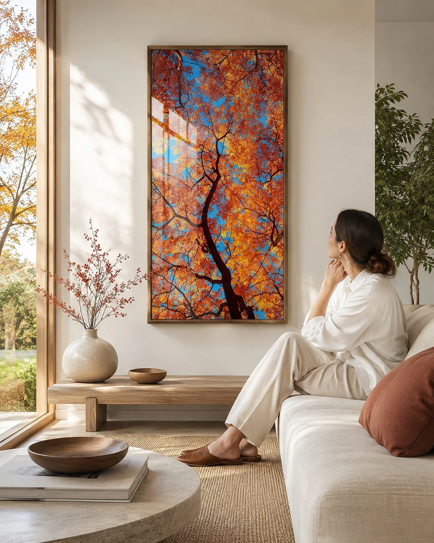 Framed autumn canopy photograph with vivid orange foliage, dark branching forms and bright blue sky in a sunlit minimalist interior with soft neutral furnishings, warm timber accents and a seated woman, by Nick Psomiadis at NIKART Studio and Gallery