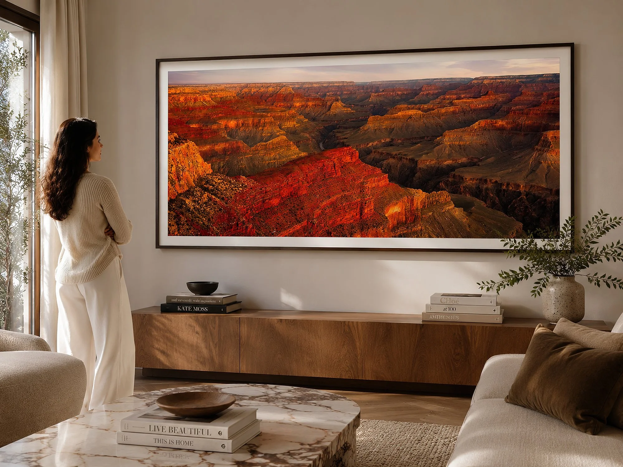 Framed panoramic Grand Canyon photograph displayed in a warm contemporary living room with a woman standing nearby.
