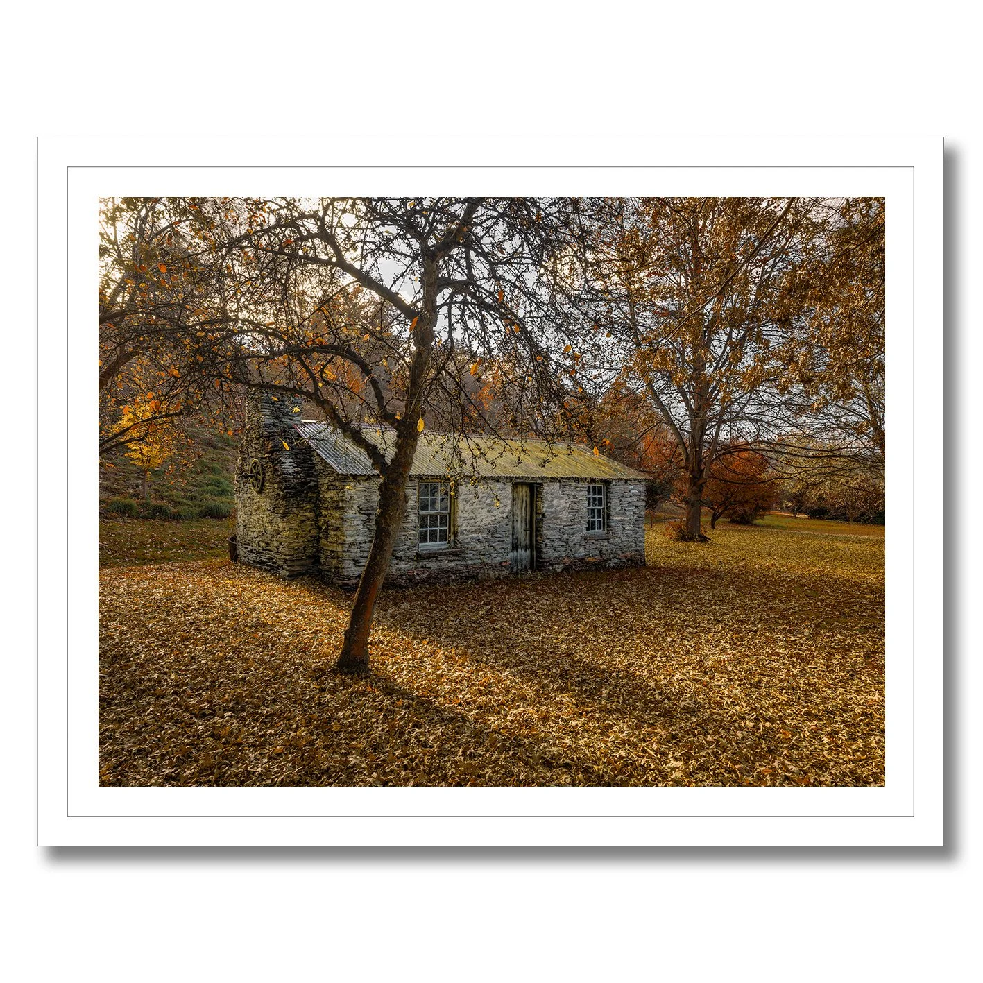 Stone cottage surrounded by autumn leaves and trees in a rural landscape photograph