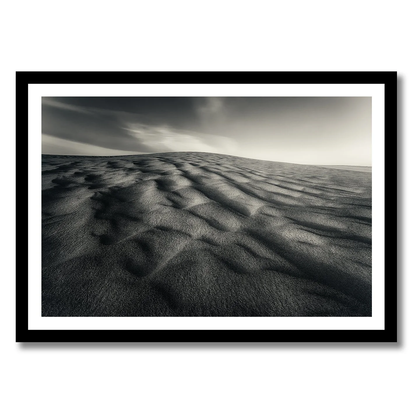 Black and white photograph of wind-sculpted sand dunes beneath a dramatic sky.