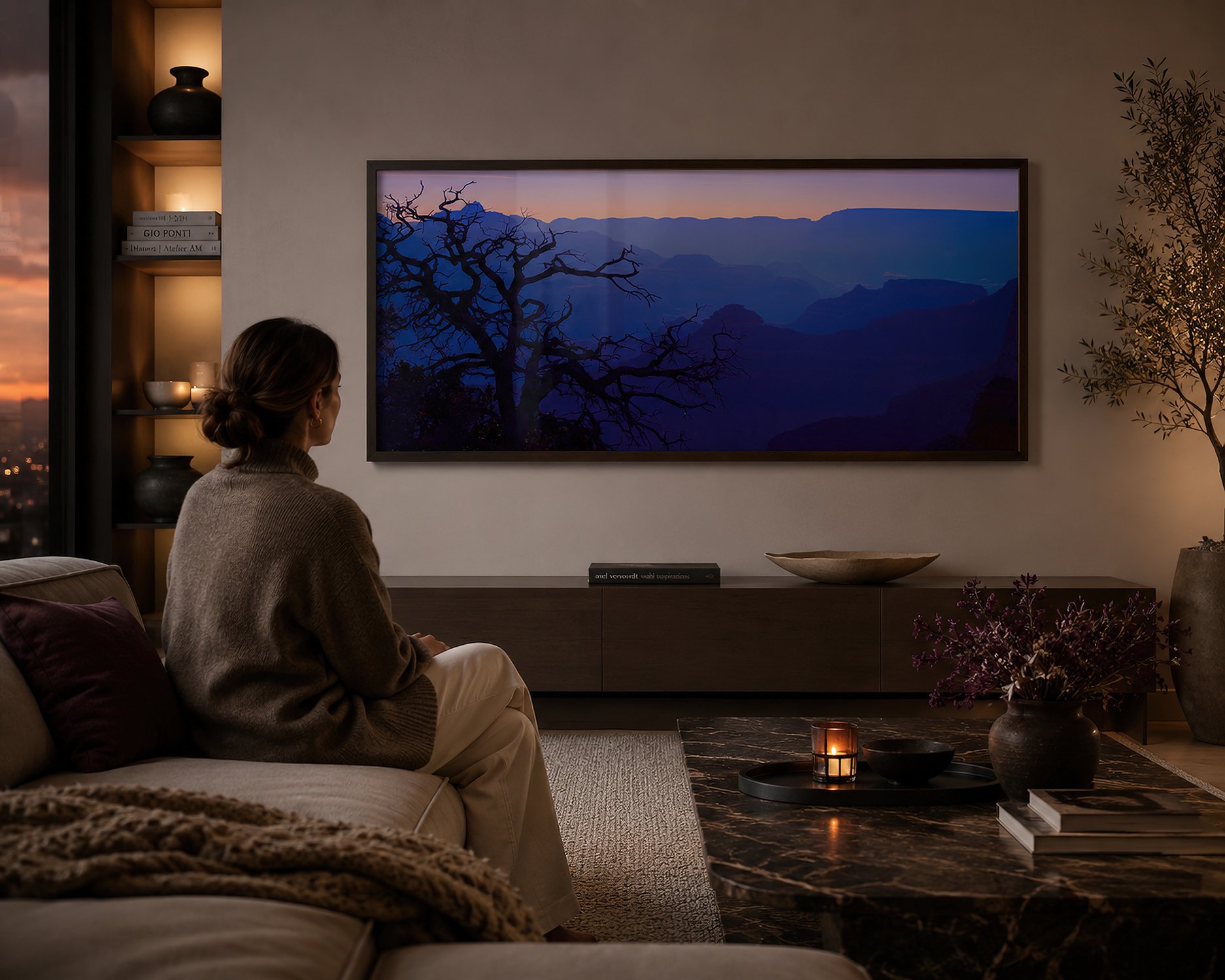 Framed Grand Canyon dawn photograph displayed behind reflective glass in a warm minimalist living room with a seated woman.