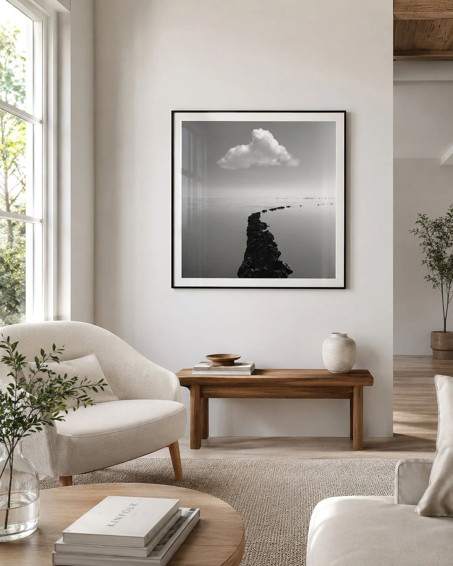 Framed square black-and-white photograph of a lone cloud above calm water, presented behind reflective glass in a bright minimalist interior with natural light, pale furnishings and timber accents, by Nick Psomiadis at NIKART Studio and Gallery