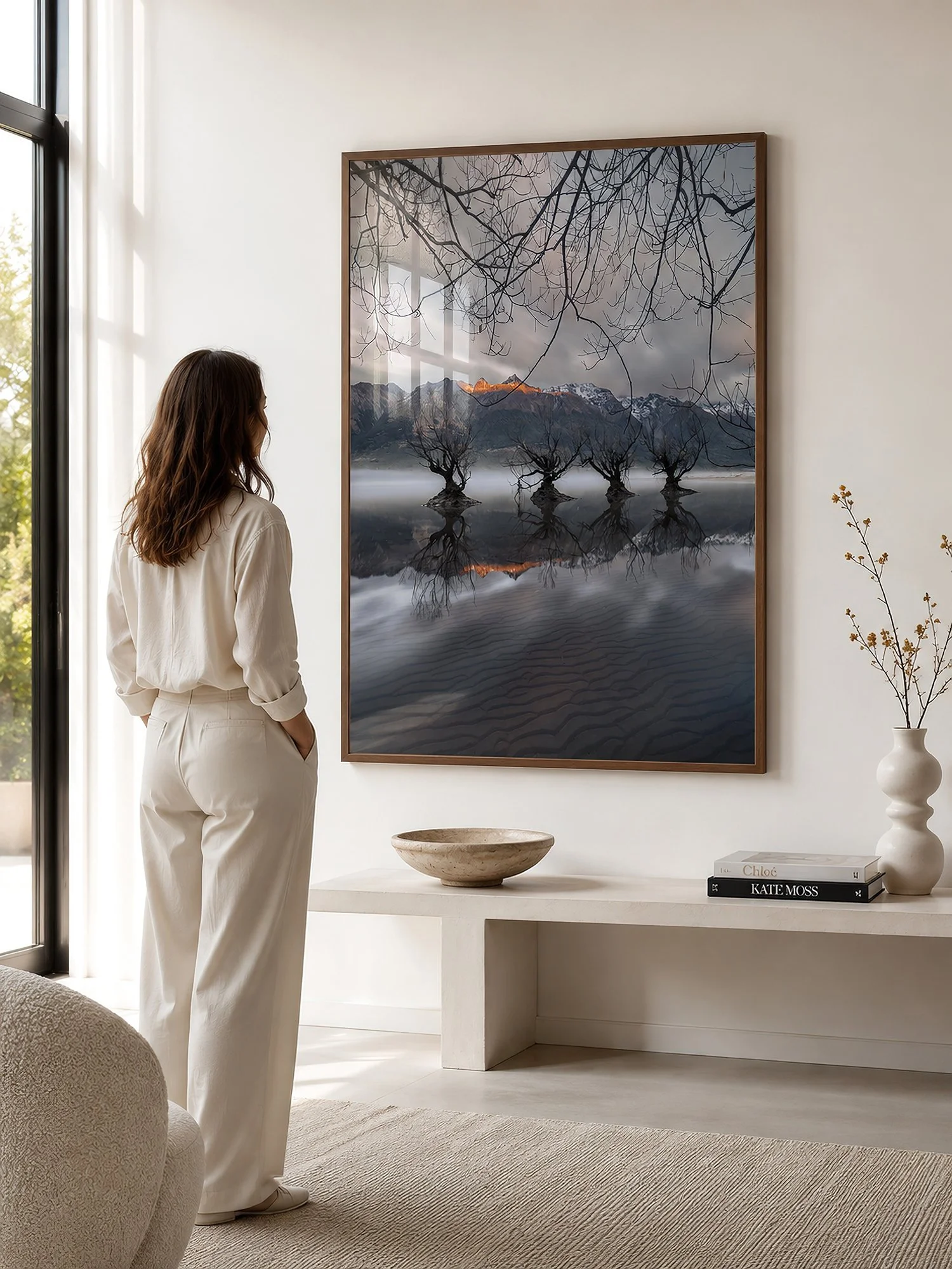 Bright minimalist interior with a woman viewing a large framed willow tree and mountain reflection photograph with glass reflections by Nick Psomiadis at NIKART Studio and Gallery