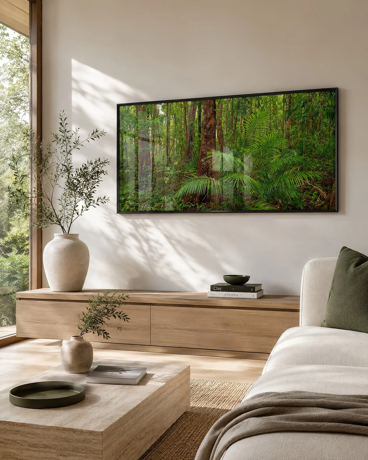 Bright minimalist living room with a framed rainforest photograph, pale timber console, stone table, greenery and soft window reflections by Nick Psomiadis at NIKART Studio and Gallery