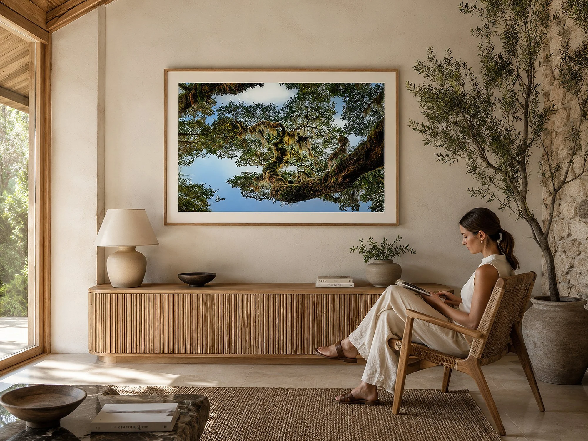 Woman reading beside a framed moss-covered forest canopy photograph in a warm natural interior with timber furniture by Nick Psomiadis at NIKART Studio and Gallery