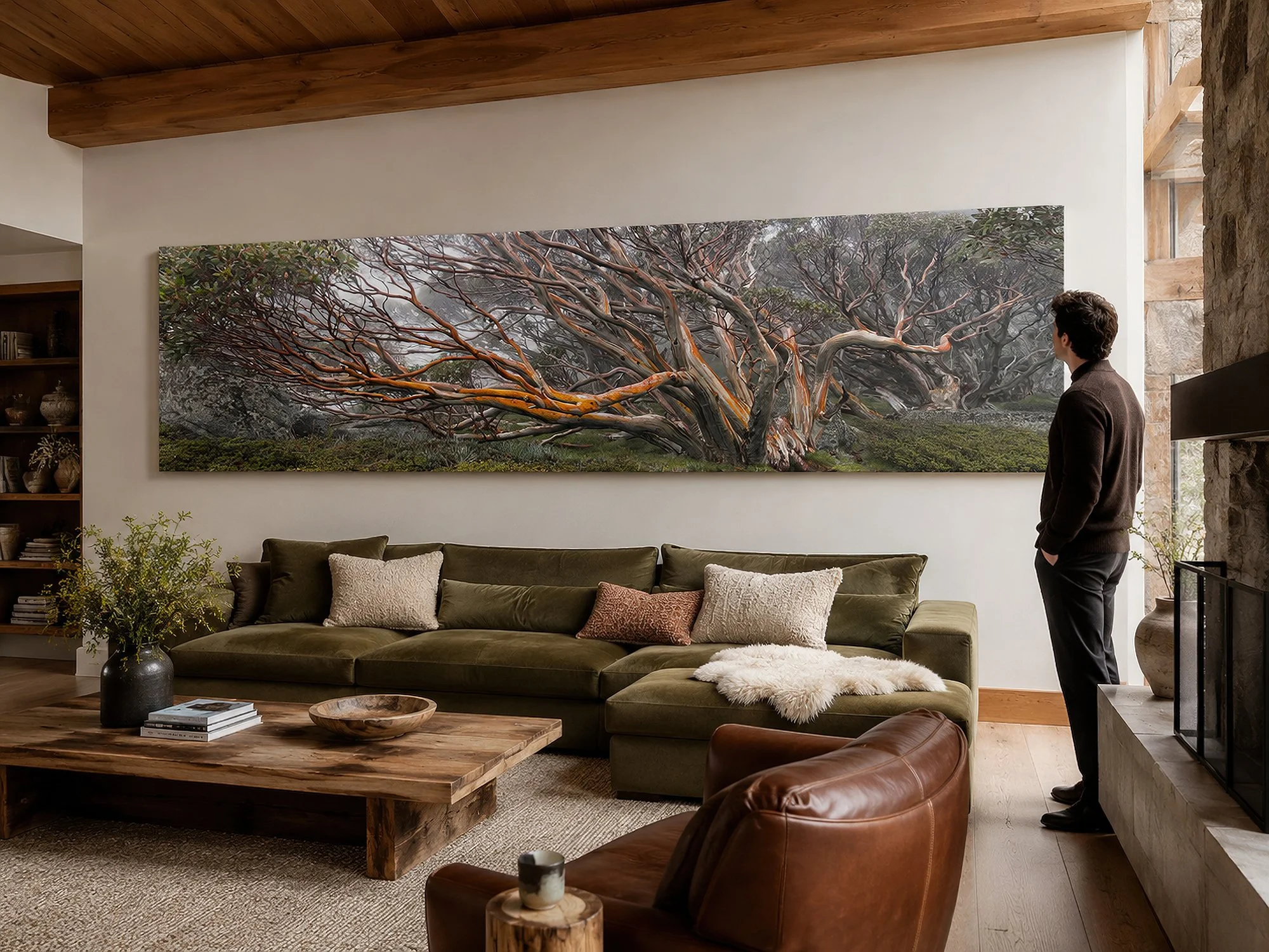 Panoramic snow gum canvas print displayed above an olive sofa in a warm rustic living room with a man viewing the artwork by Nick Psomiadis at NIKART Studio and Gallery
