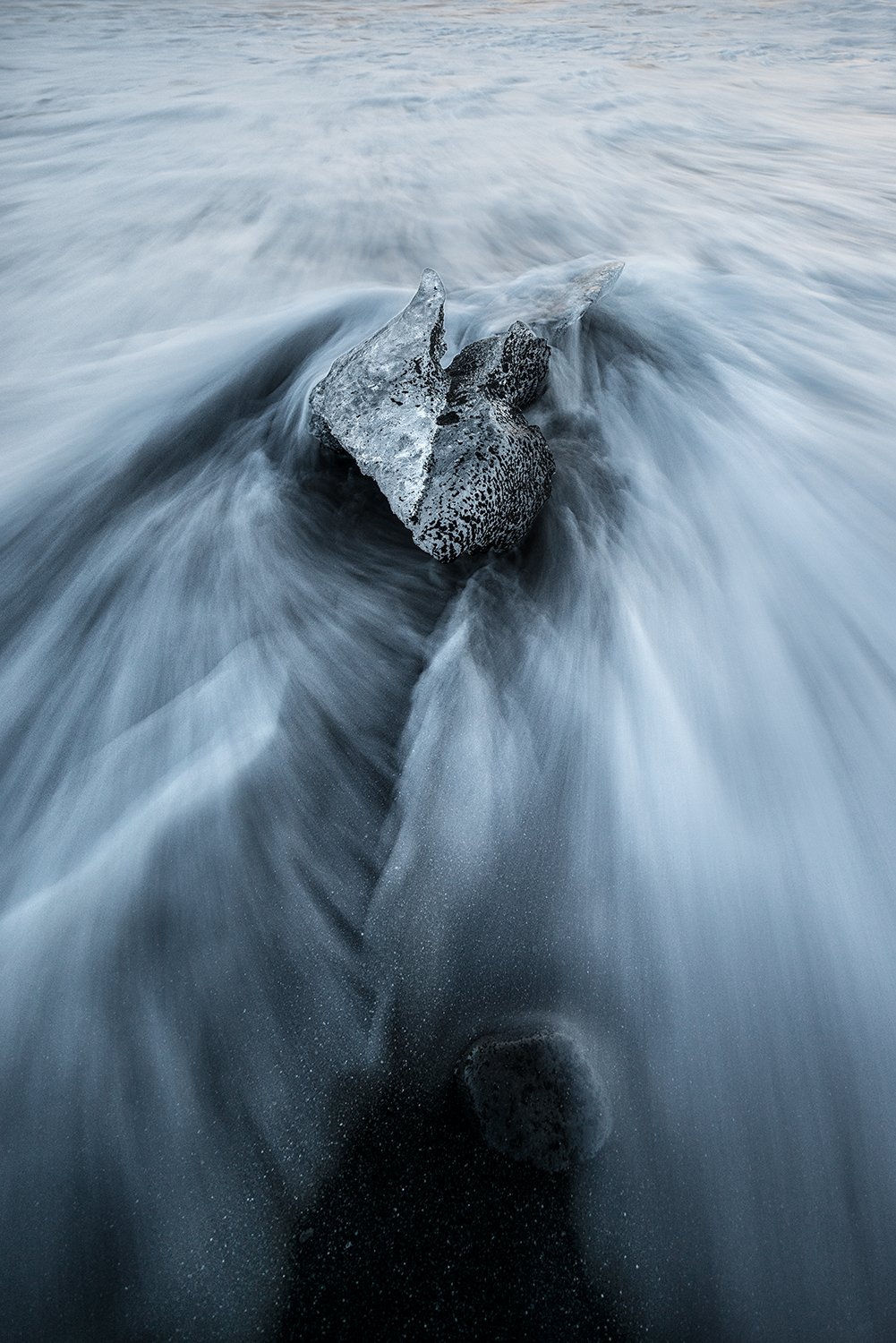 Ice fragment on black sand with flowing water, Iceland coastal photograph