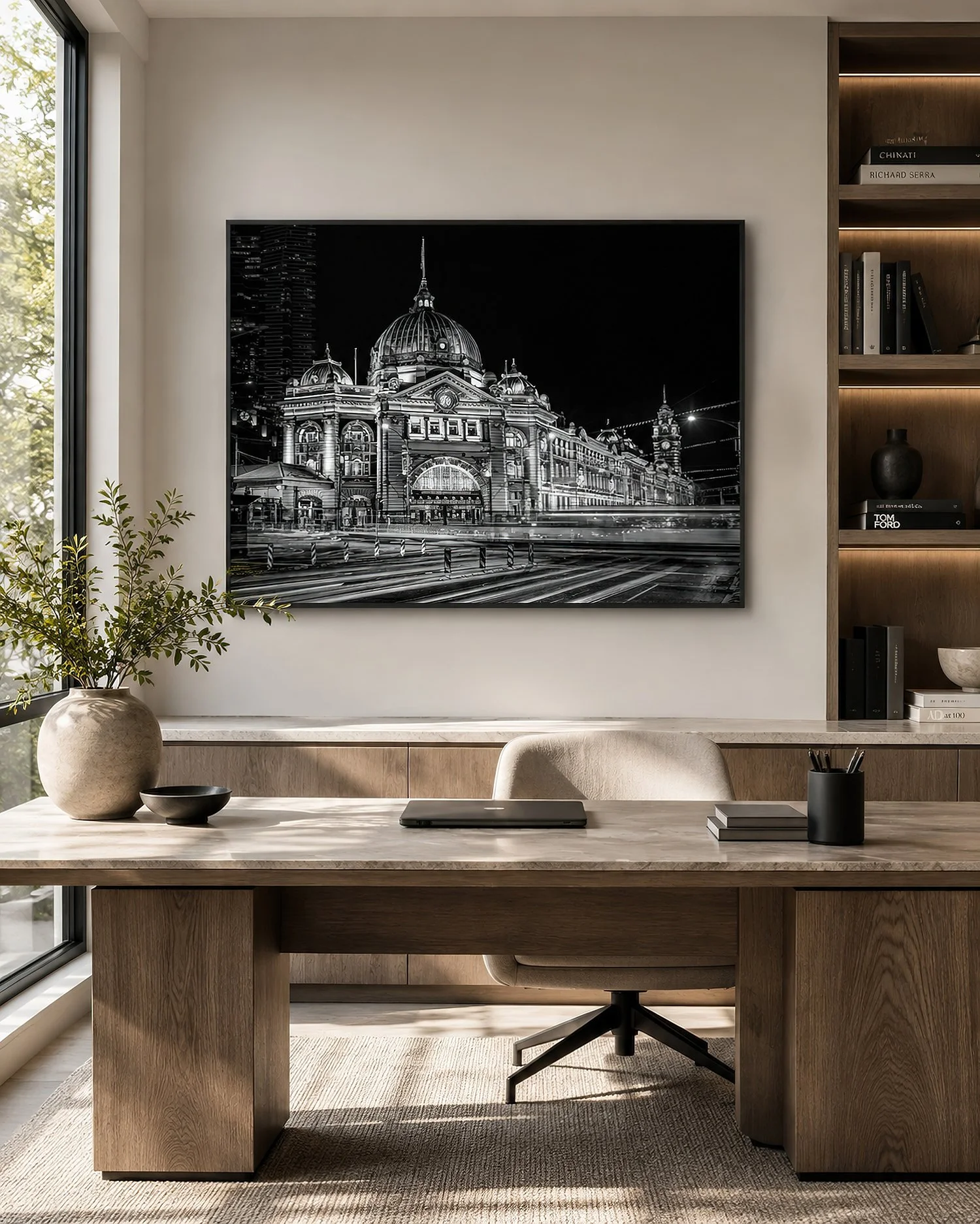 Framed black-and-white Flinders Street Station photograph with illuminated architecture and light trails in a sunlit minimalist study with warm timber furniture and shelving, by Nick Psomiadis at NIKART Studio and Gallery