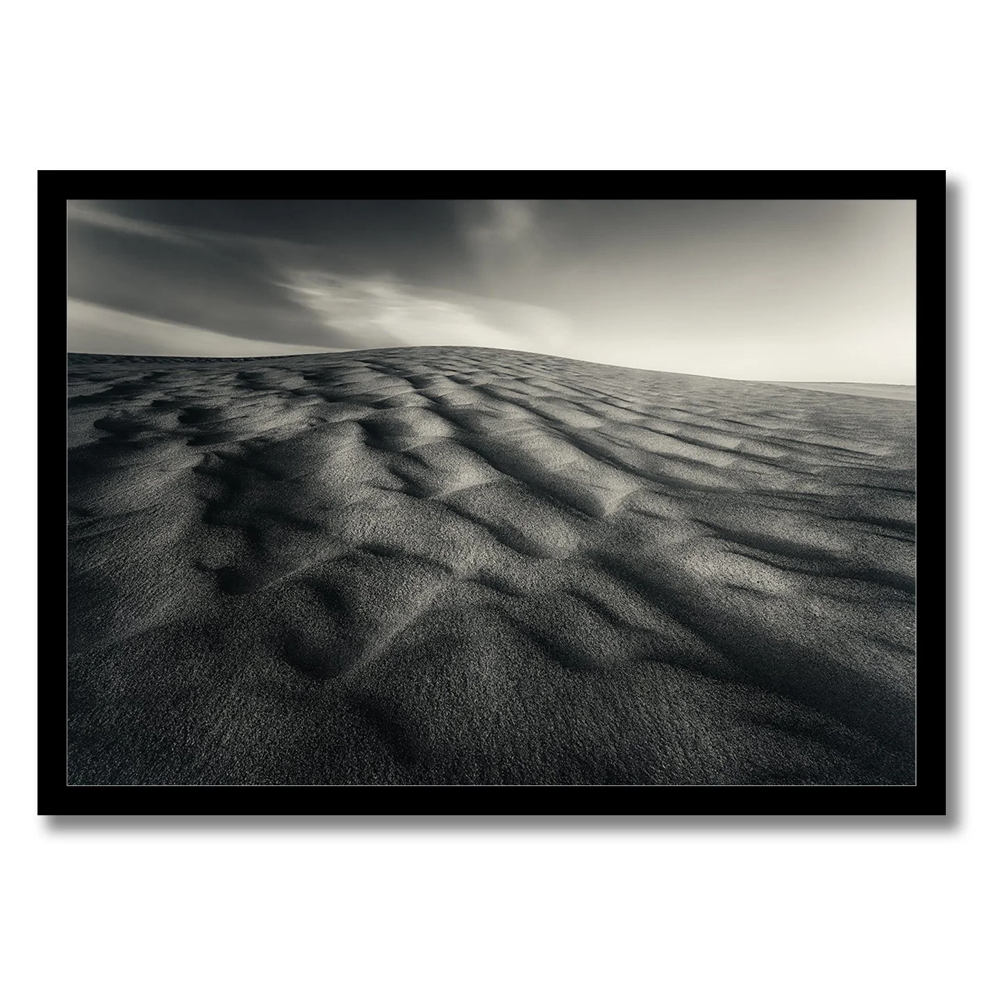 Black and white photograph of wind-sculpted sand dunes beneath a dramatic sky.