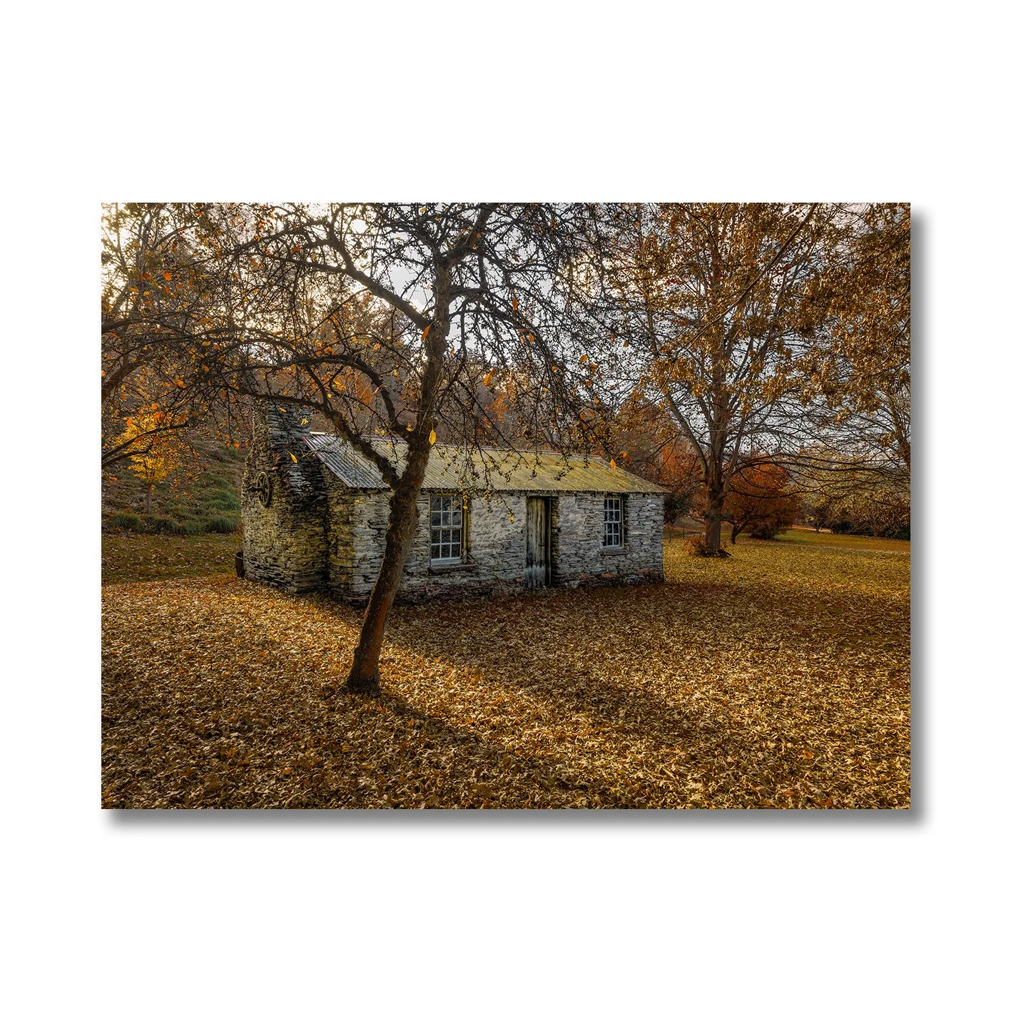 Stone cottage surrounded by autumn leaves and trees in a rural landscape photograph