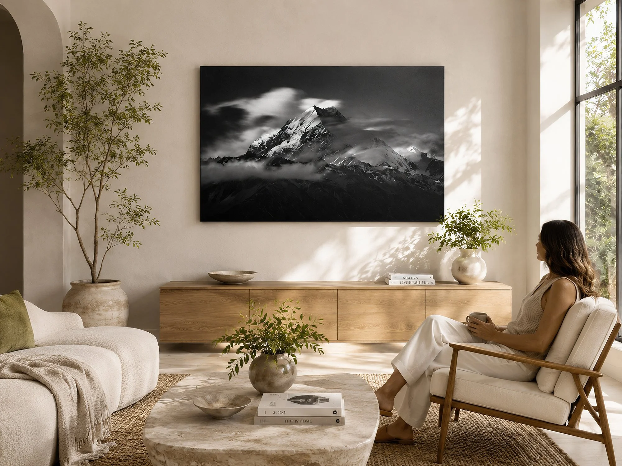 Monochrome mountain canvas print in a bright organic modern living room with arched architecture, natural timber furniture and a seated woman by Nick Psomiadis at NIKART Studio and Gallery