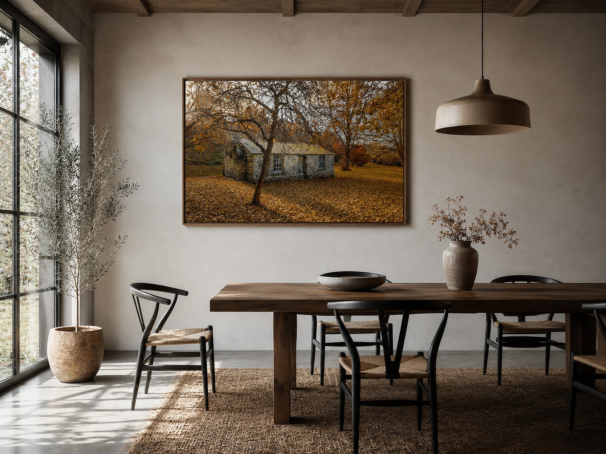 Framed autumn stone cottage photograph displayed in a bright rustic-modern dining room with a timber table, woven chairs and soft natural light by Nick Psomiadis at NIKART Studio and Gallery