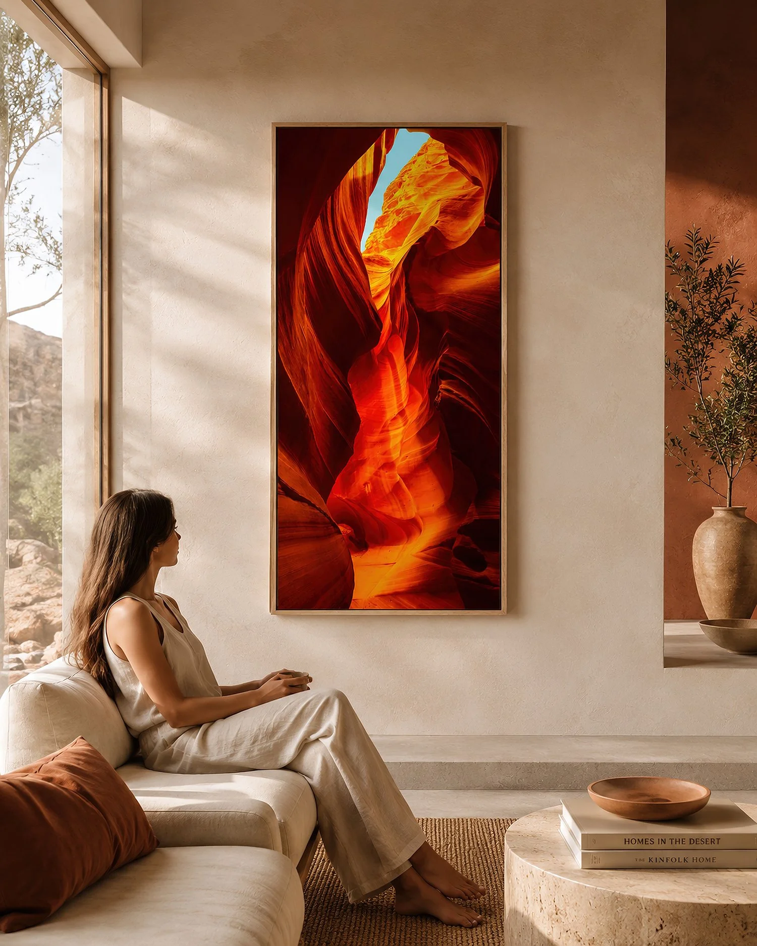 Framed vertical Antelope Canyon photograph in vivid orange and red tones above a beige sofa in a sunlit minimalist interior with a seated woman and terracotta décor, by Nick Psomiadis at NIKART Studio and Gallery