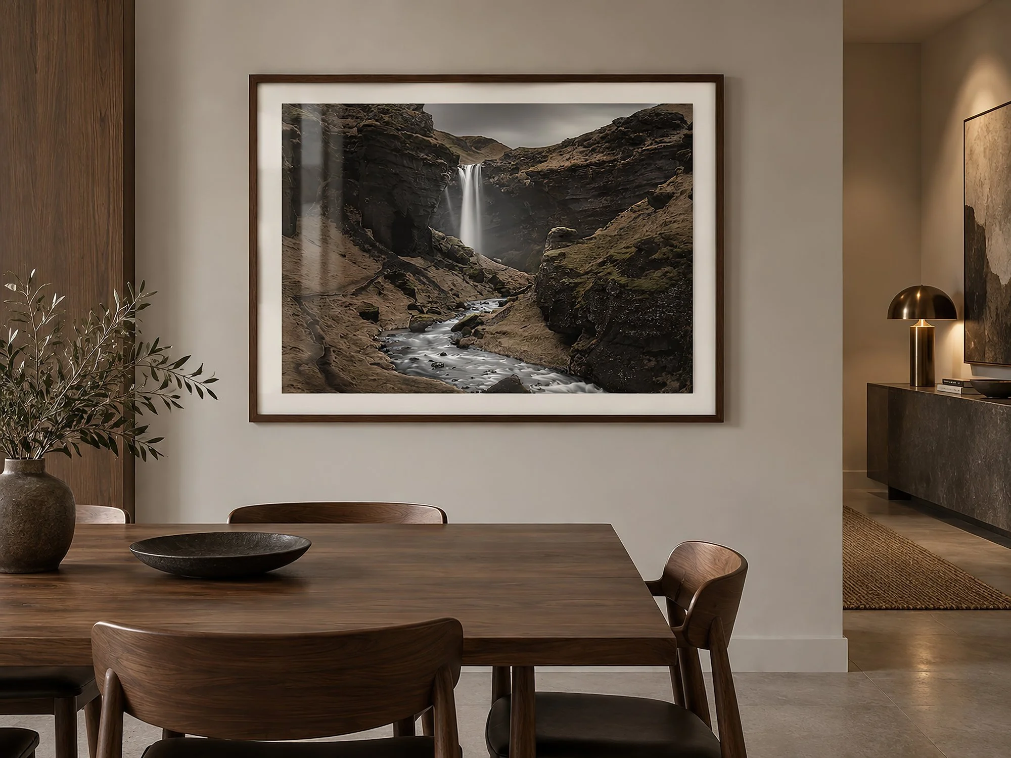Iceland waterfall photograph with dark volcanic cliffs and flowing water, framed in stained timber with an off-white mat above a modern timber dining setting, by Nick Psomiadis at NIKART Studio and Gallery
