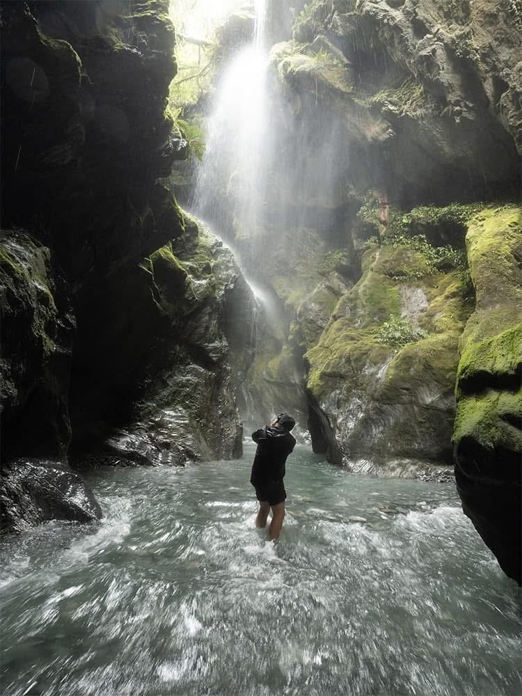 Photographer standing in flowing canyon water beneath dramatic waterfall photography scene