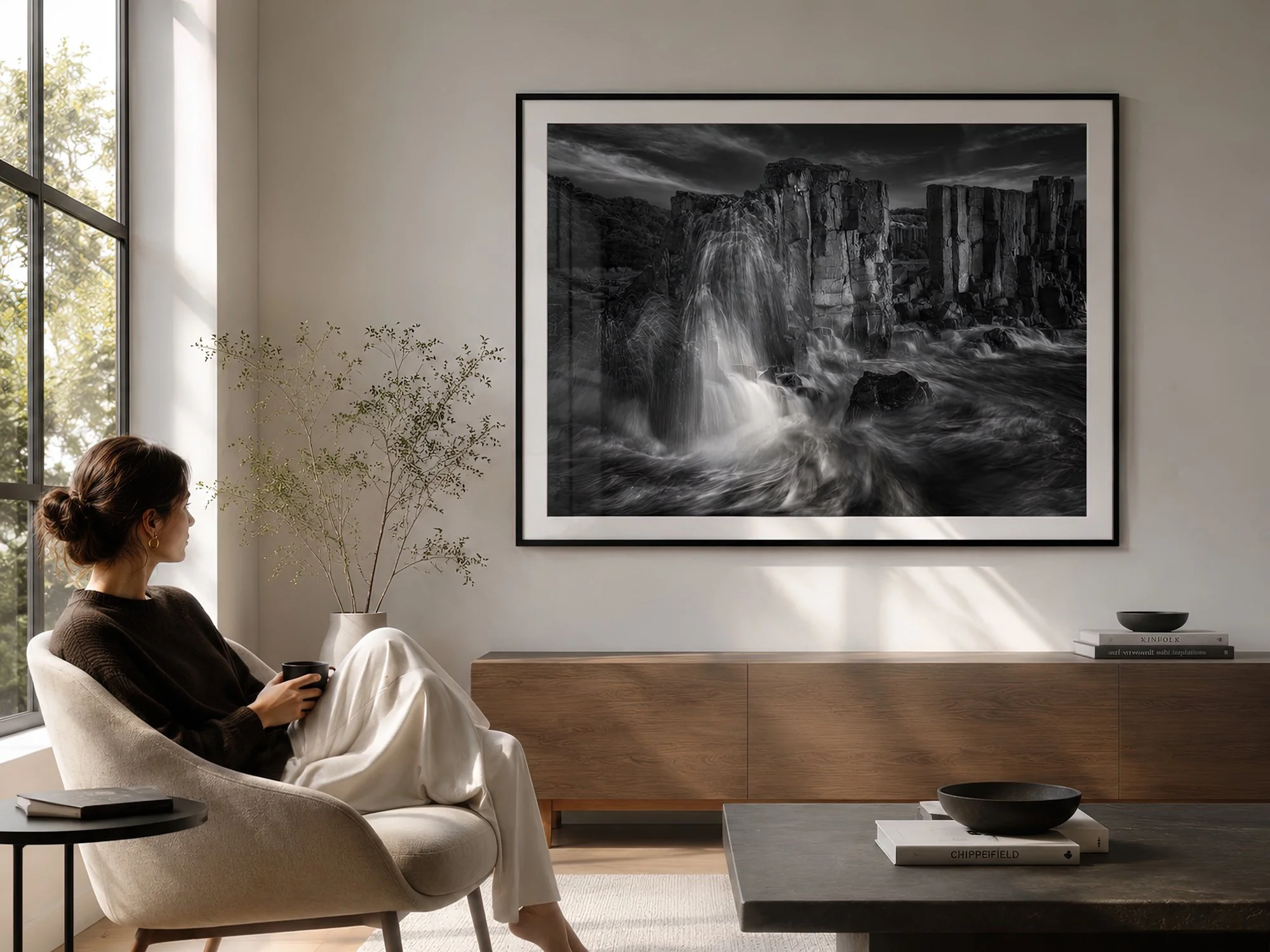 Bright minimalist living room with a seated woman beside a black-framed monochrome Bombo Quarry seascape photograph with natural glass reflections by Nick Psomiadis at NIKART Studio and Gallery
