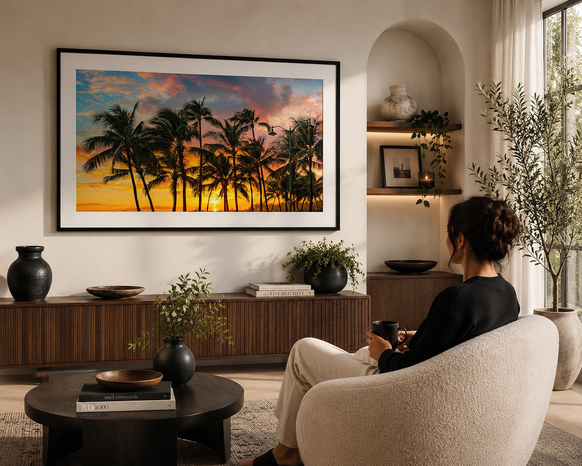 Framed Hawaiian sunset photograph displayed in a warm contemporary lounge with a seated woman holding a mug.