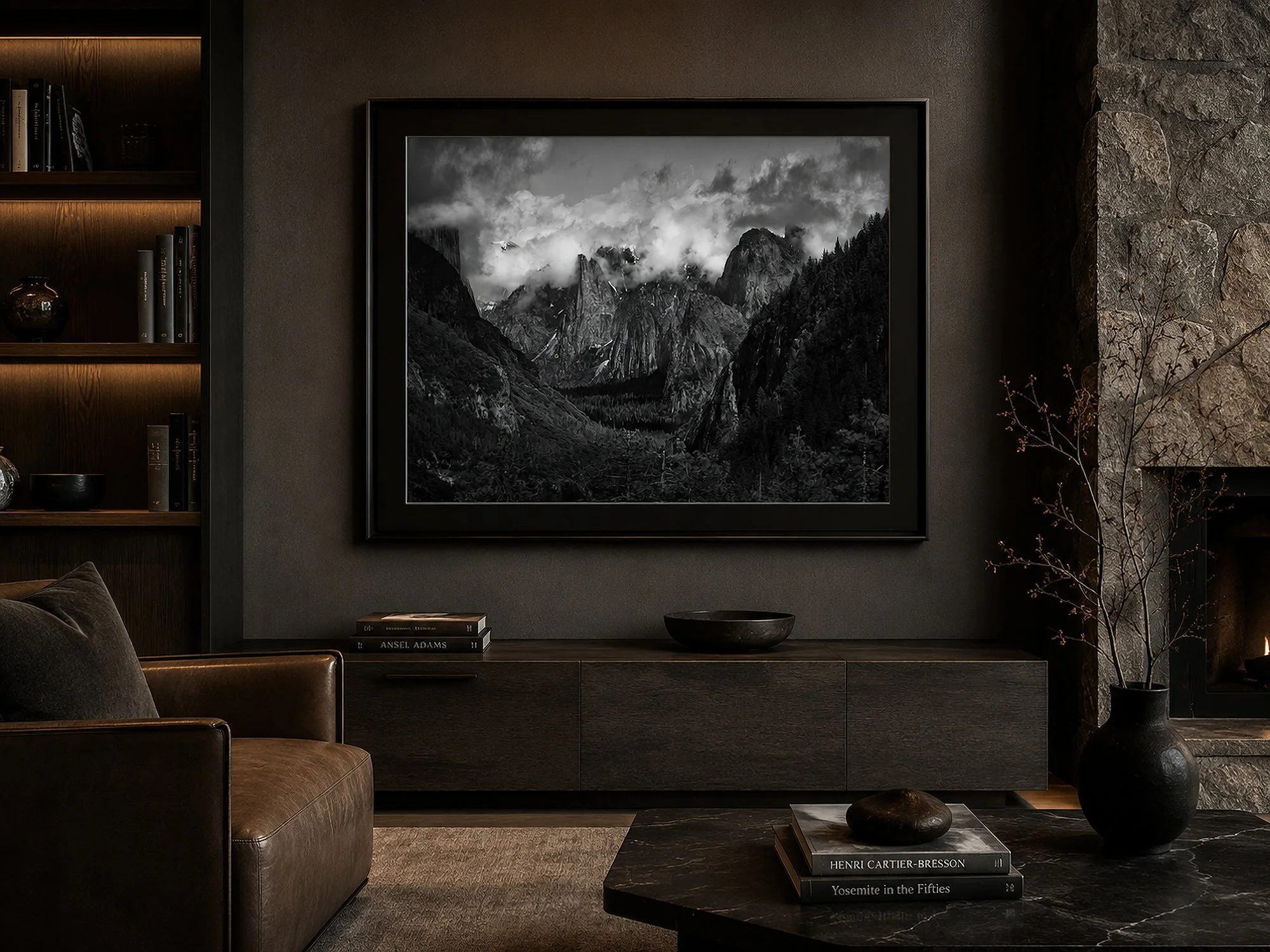 Framed black-and-white Yosemite photograph with a black mat displayed in a sophisticated dark living room with a stone fireplace.
