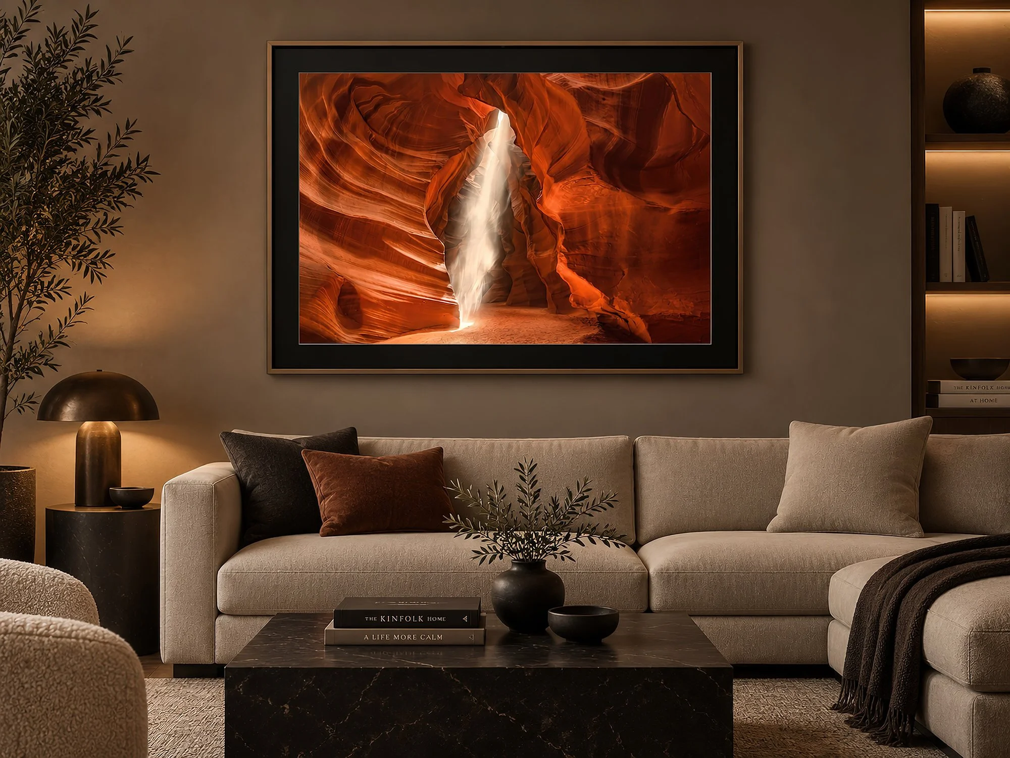 Minimalist lounge with warm moody lighting, neutral sofa and dark stone table, featuring a framed Antelope Canyon photograph with glowing sandstone walls and a dramatic beam of light by Nick Psomiadis at NIKART Studio and Gallery