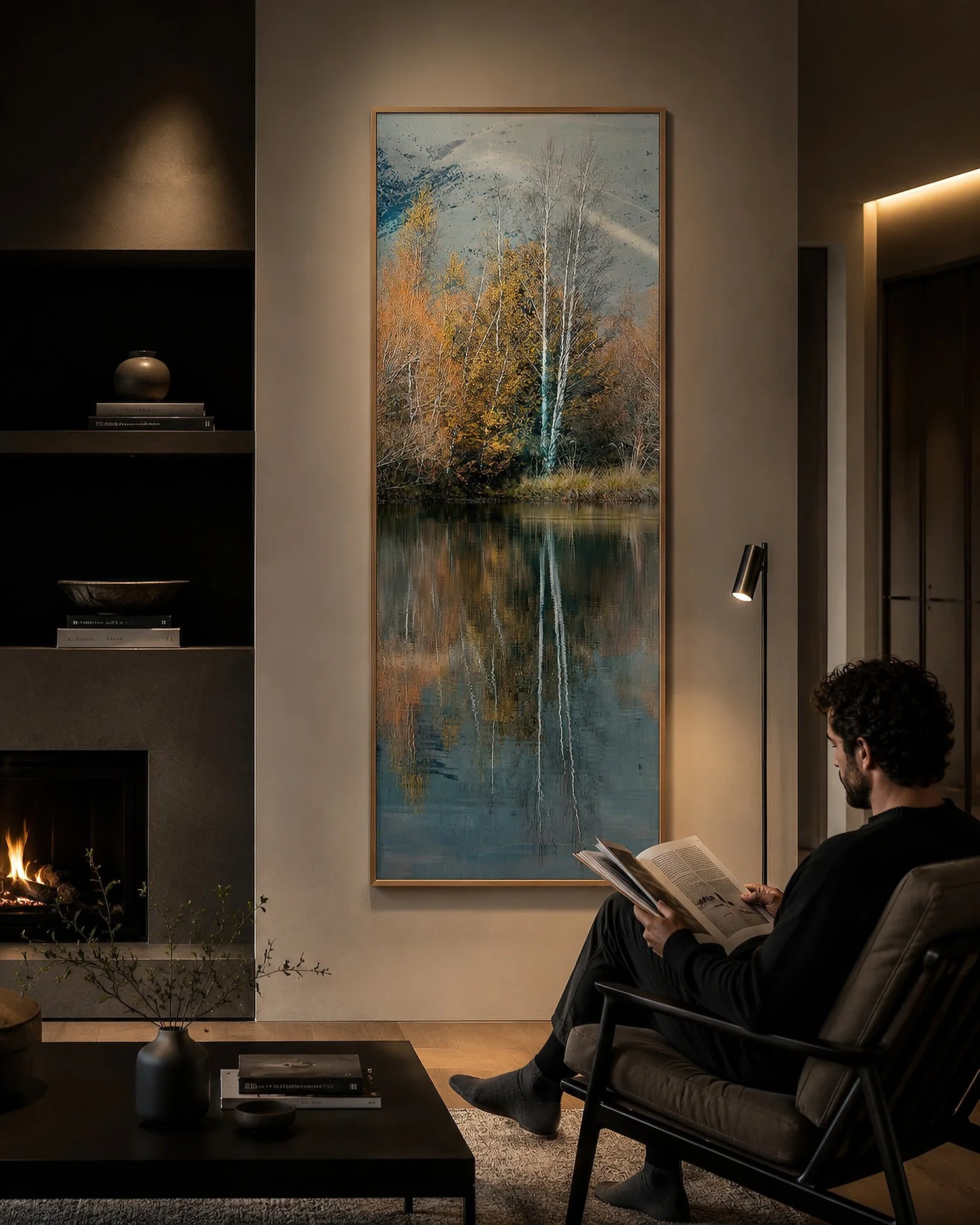Moody modern minimalist living room with a tall framed autumn landscape photograph, featuring golden trees reflected in calm blue water, beside a seated reader, by Nick Psomiadis at NIKART Studio and Gallery