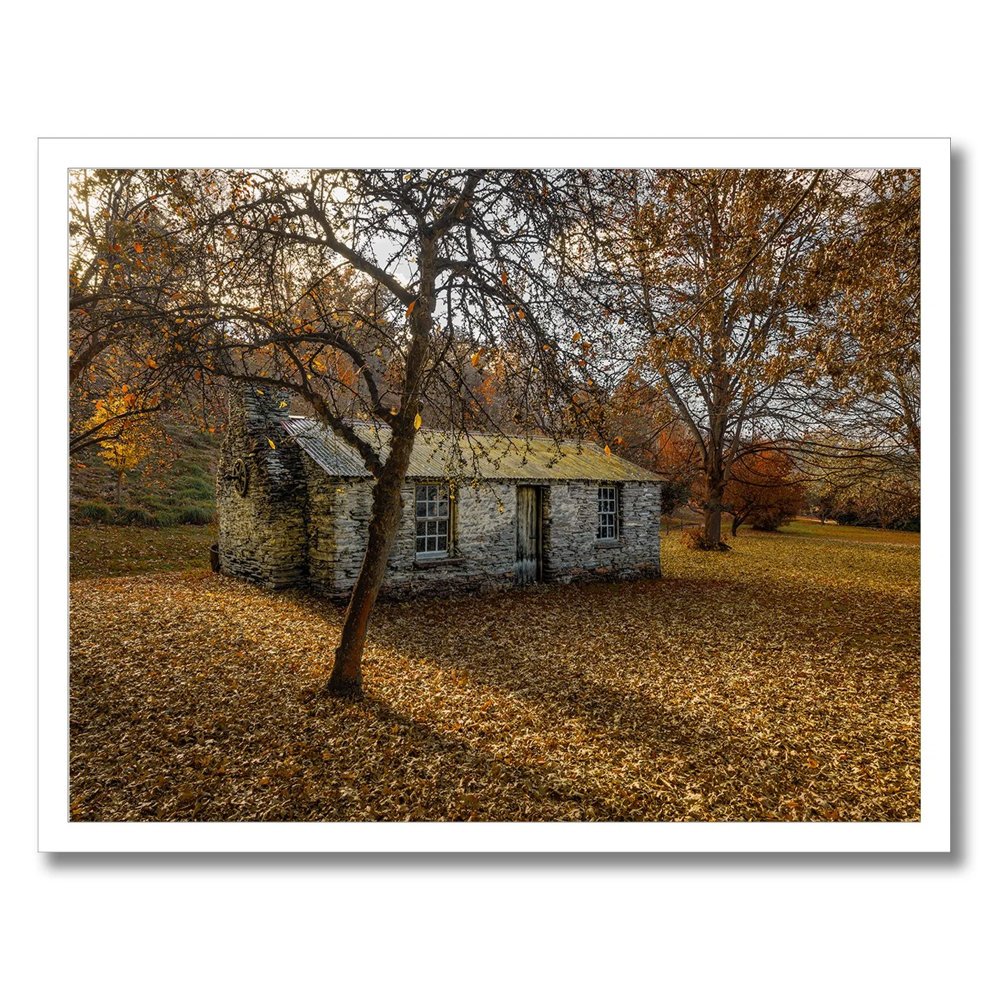 Stone cottage surrounded by autumn leaves and trees in a rural landscape photograph