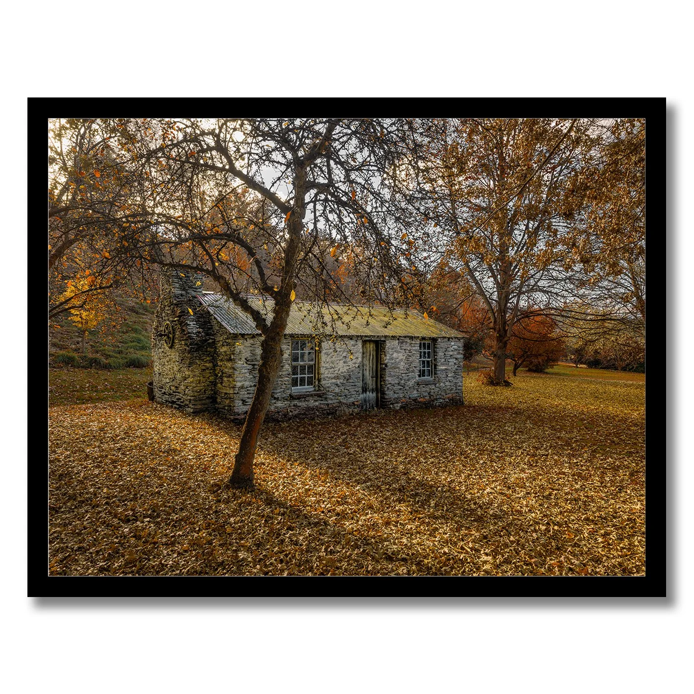 Stone cottage surrounded by autumn leaves and trees in a rural landscape photograph