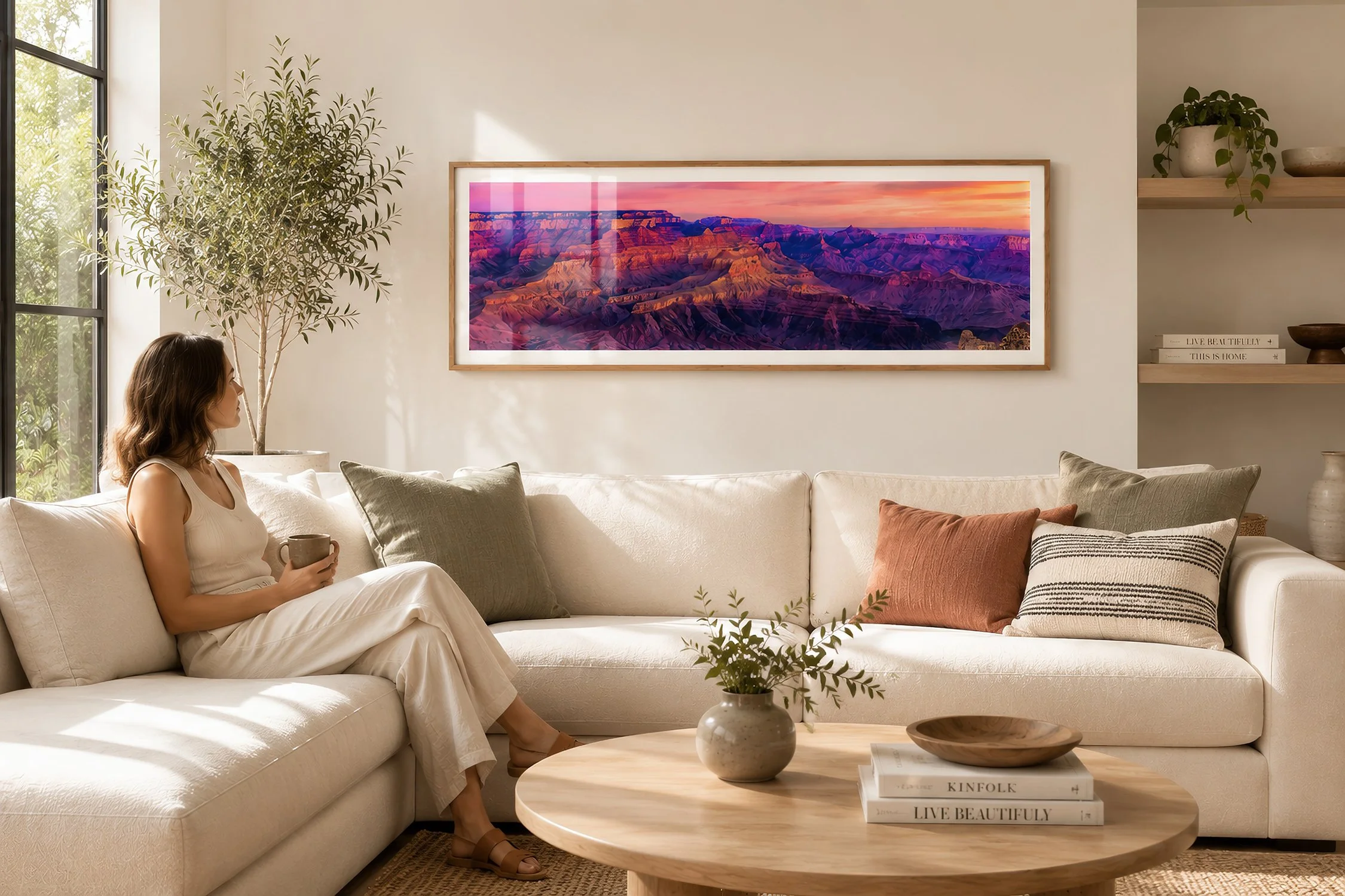 Framed panoramic Grand Canyon photograph with vivid purple cliffs and a glowing pink-orange sunset in a sunlit cream living room with warm timber, greenery and a seated woman, by Nick Psomiadis at NIKART Studio and Gallery