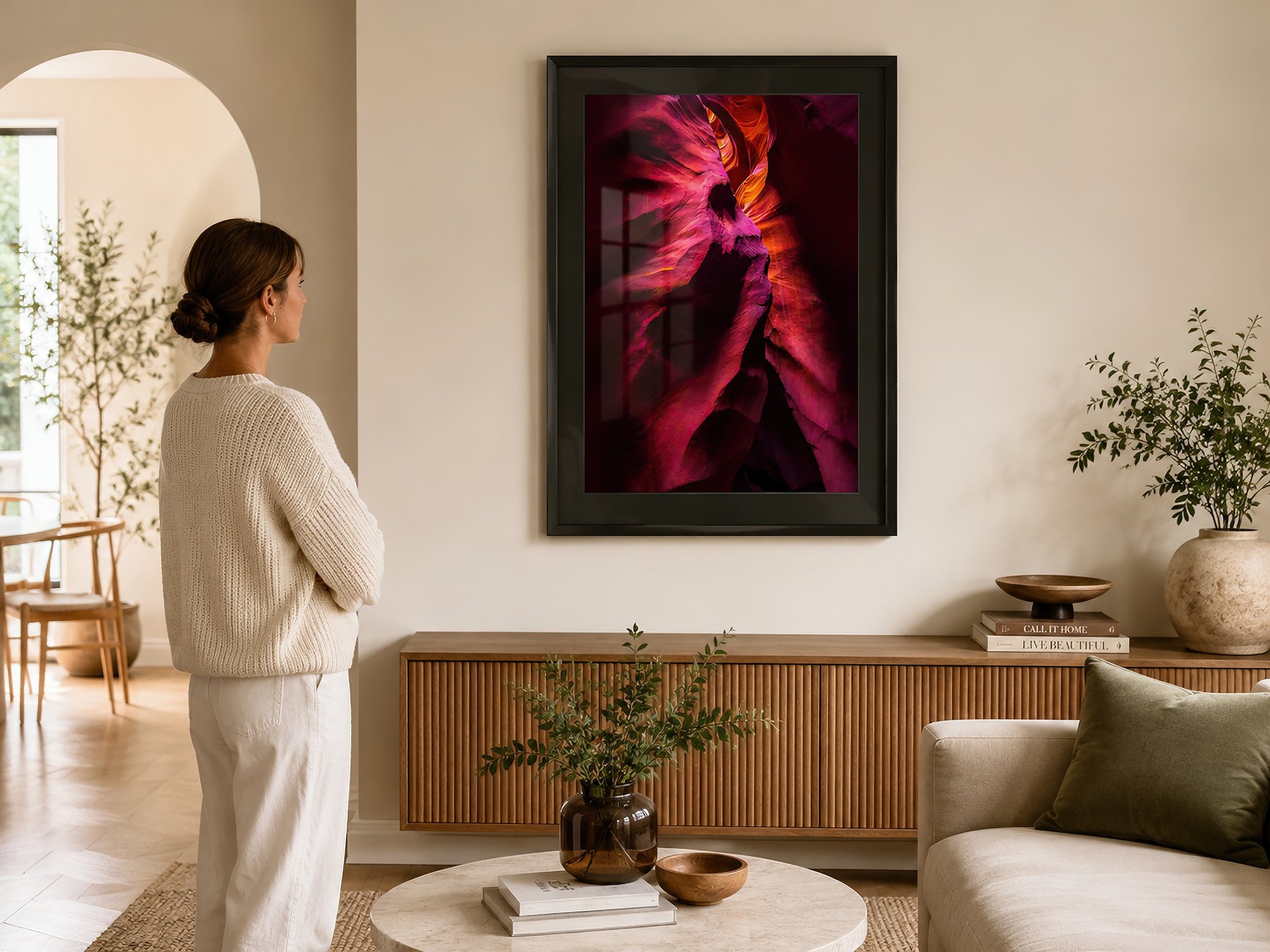 Framed Antelope Canyon photograph with a black mat displayed behind reflective glass in a bright Scandinavian-style living room with a woman standing beside a timber console — Nick Psomiadis at NIKART Studio and Gallery.
