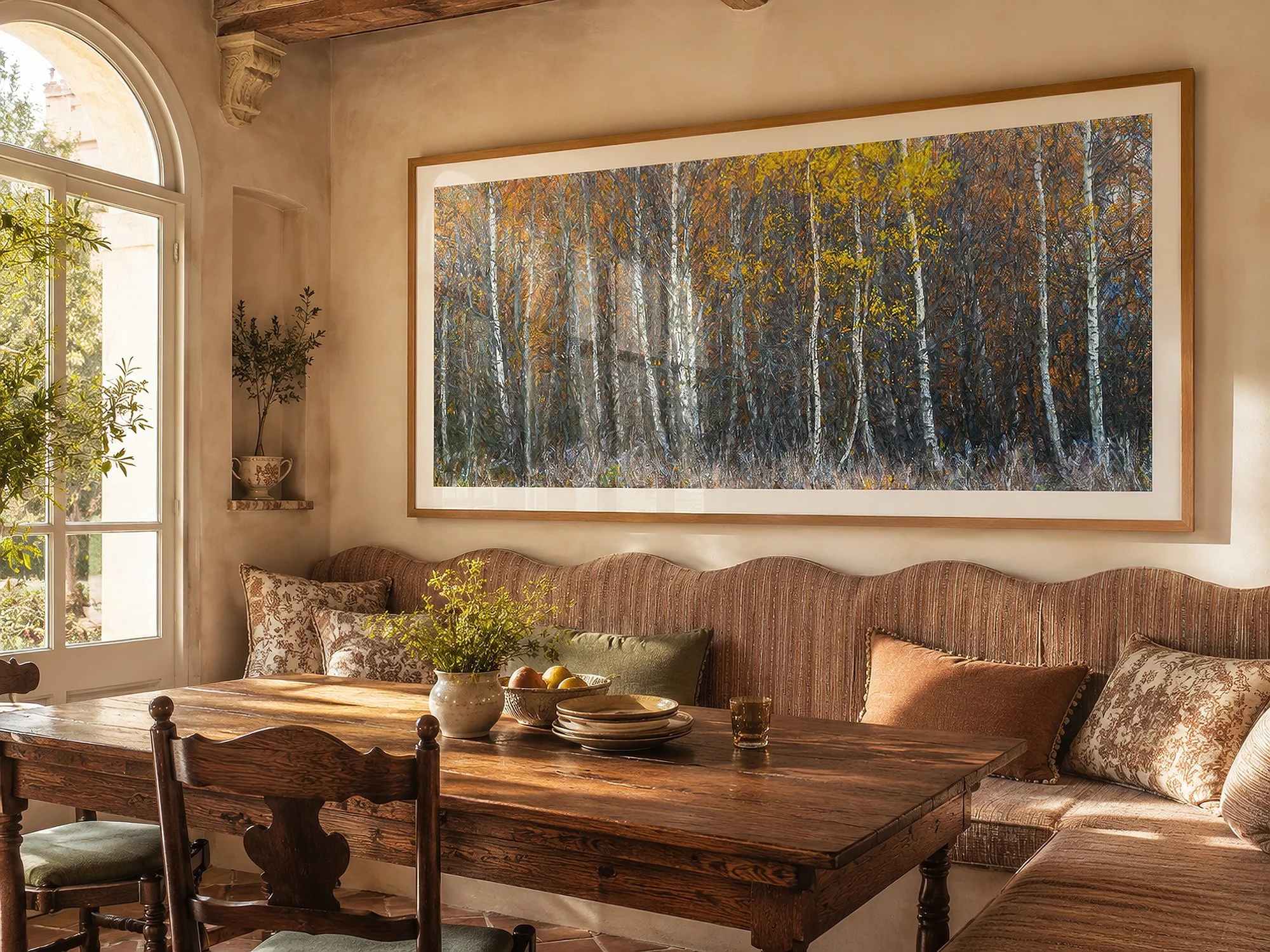 Large framed panoramic autumn forest photograph displayed in a sunlit Mediterranean-style dining nook with rustic timber furniture and warm earthy textiles by Nick Psomiadis at NIKART Studio and Gallery