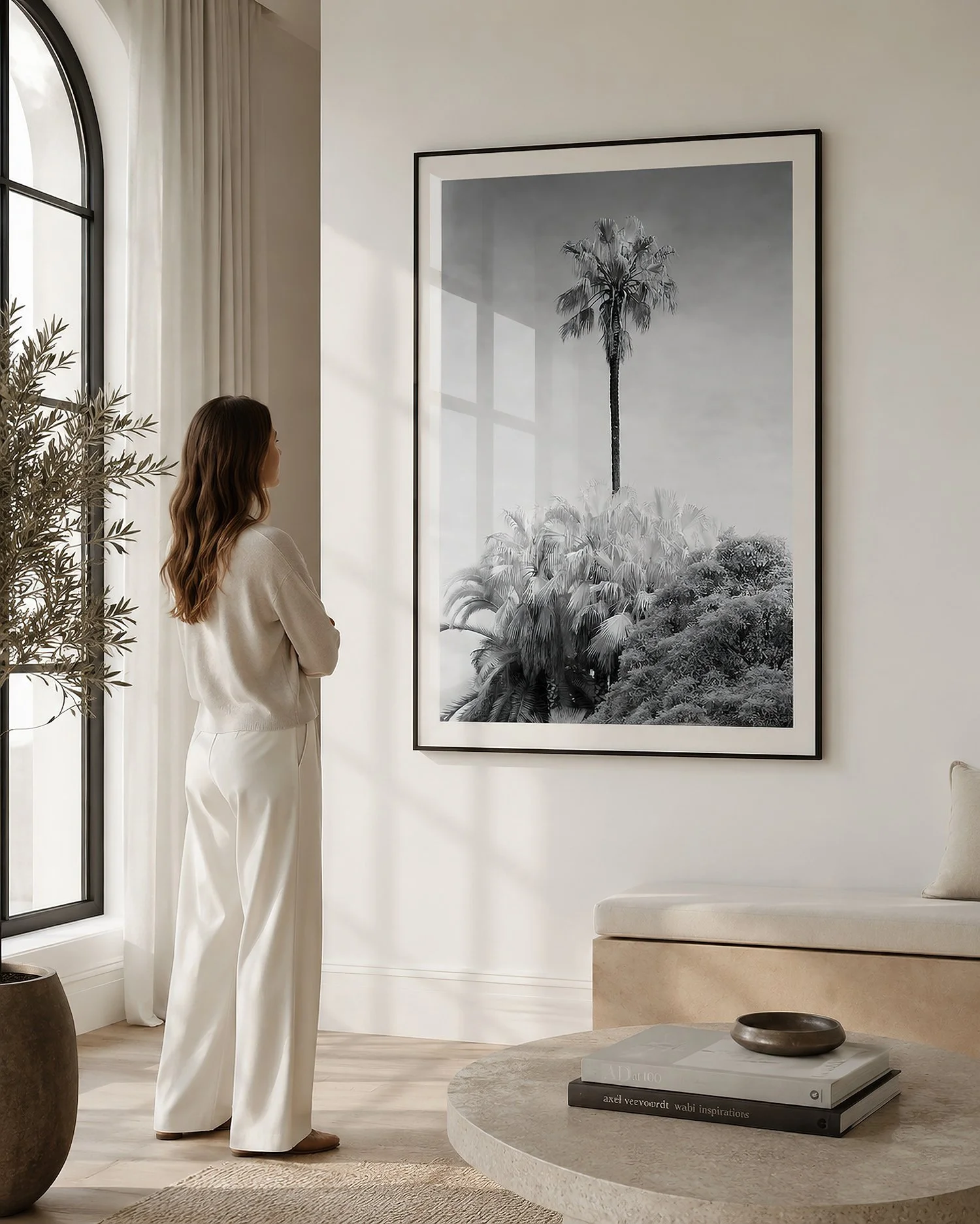 Bright minimalist living room with a woman viewing a black-framed monochrome palm tree photograph with a white mat and glass reflections by Nick Psomiadis at NIKART Studio and Gallery