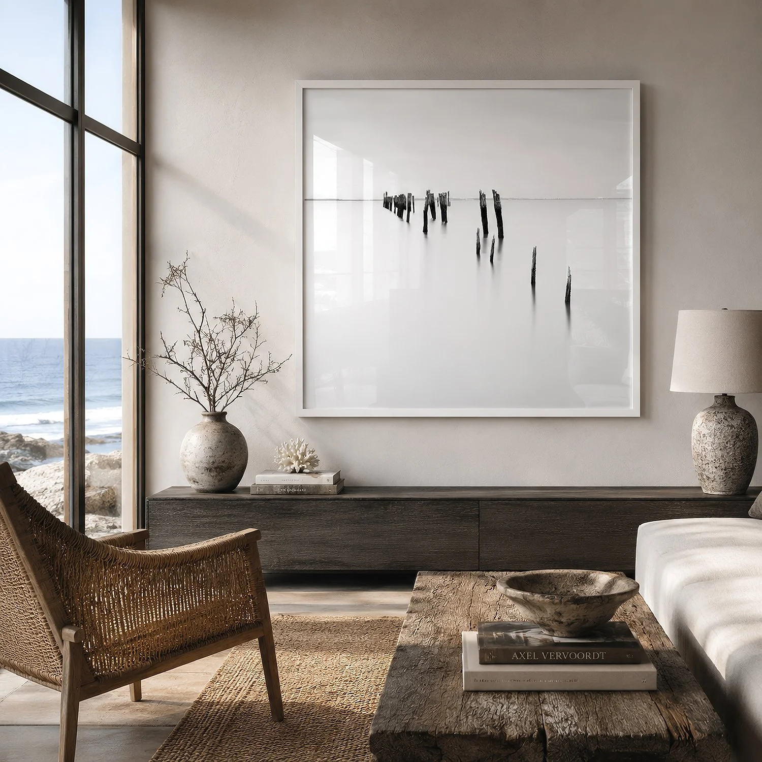 Coastal living room featuring a square white-framed black and white photograph of weathered pylons in still water, with soft interior reflections on the glass, by Nick Psomiadis at NIKART Studio and Gallery.