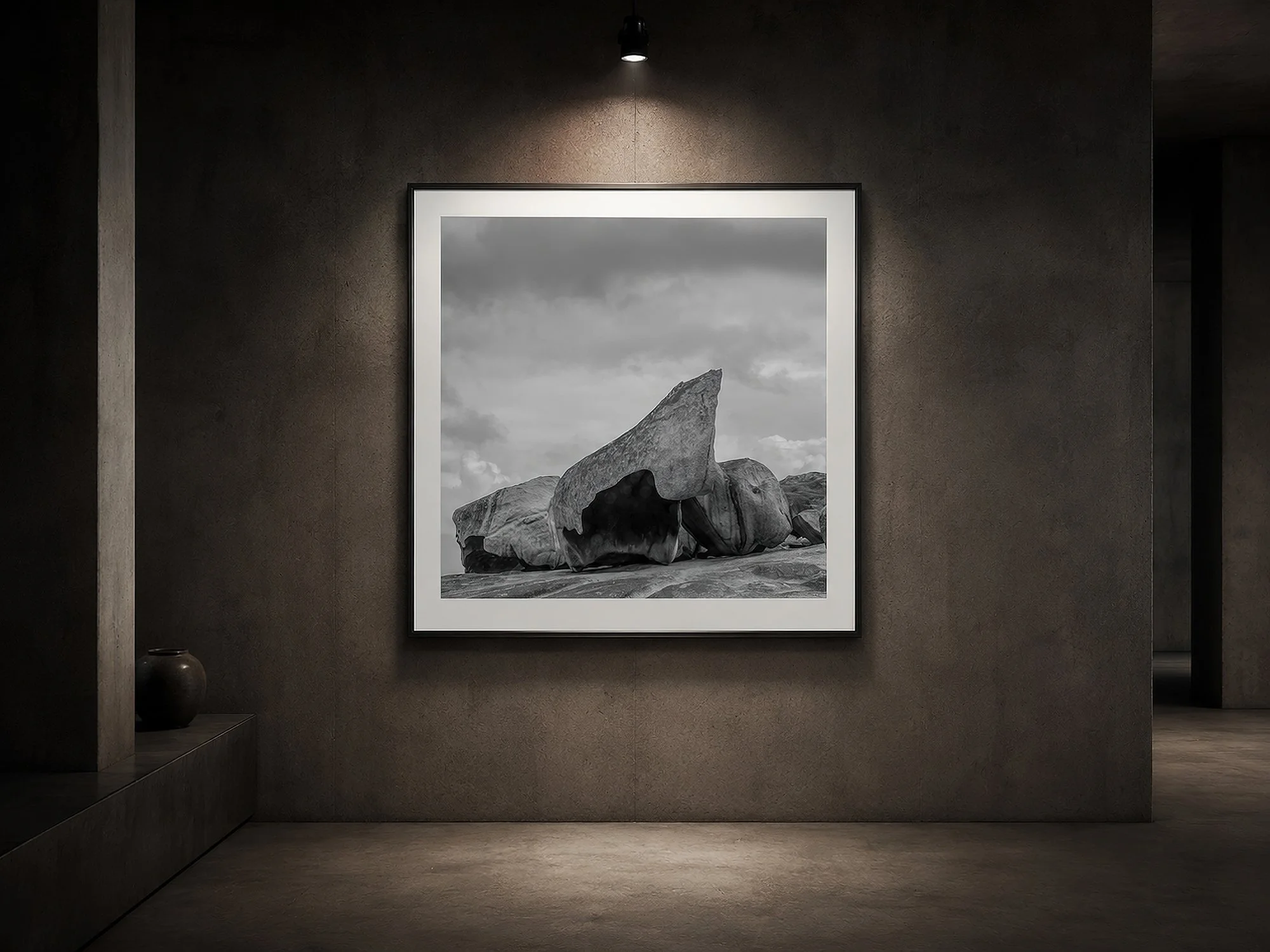 Framed black-and-white rock formation photograph illuminated by a gallery spotlight in a dark concrete interior by Nick Psomiadis at NIKART Studio and Gallery