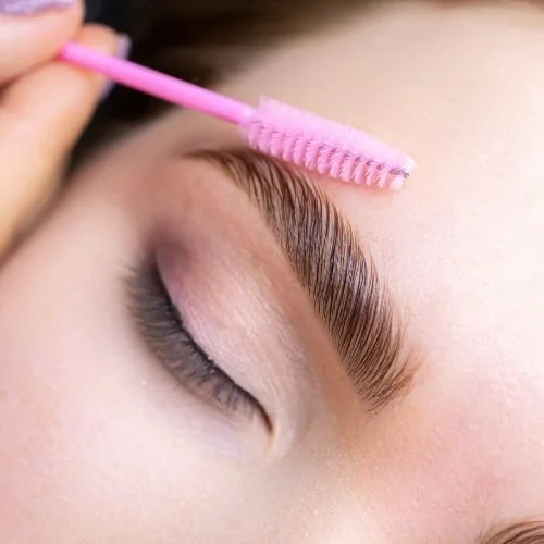 Close-up of a well-groomed brow being brushed with a clean pink spoolie brush, illustrating proper care to keep brows clean and dry during the first two weeks of the healing process after a nano brow treatment.