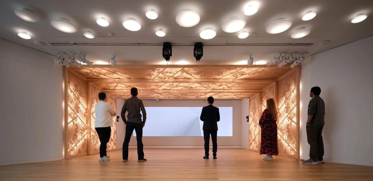 Five people standing and looking at a large blank digital screen in a modern, well-lit room with decorative wooden walls and a wood ceiling.