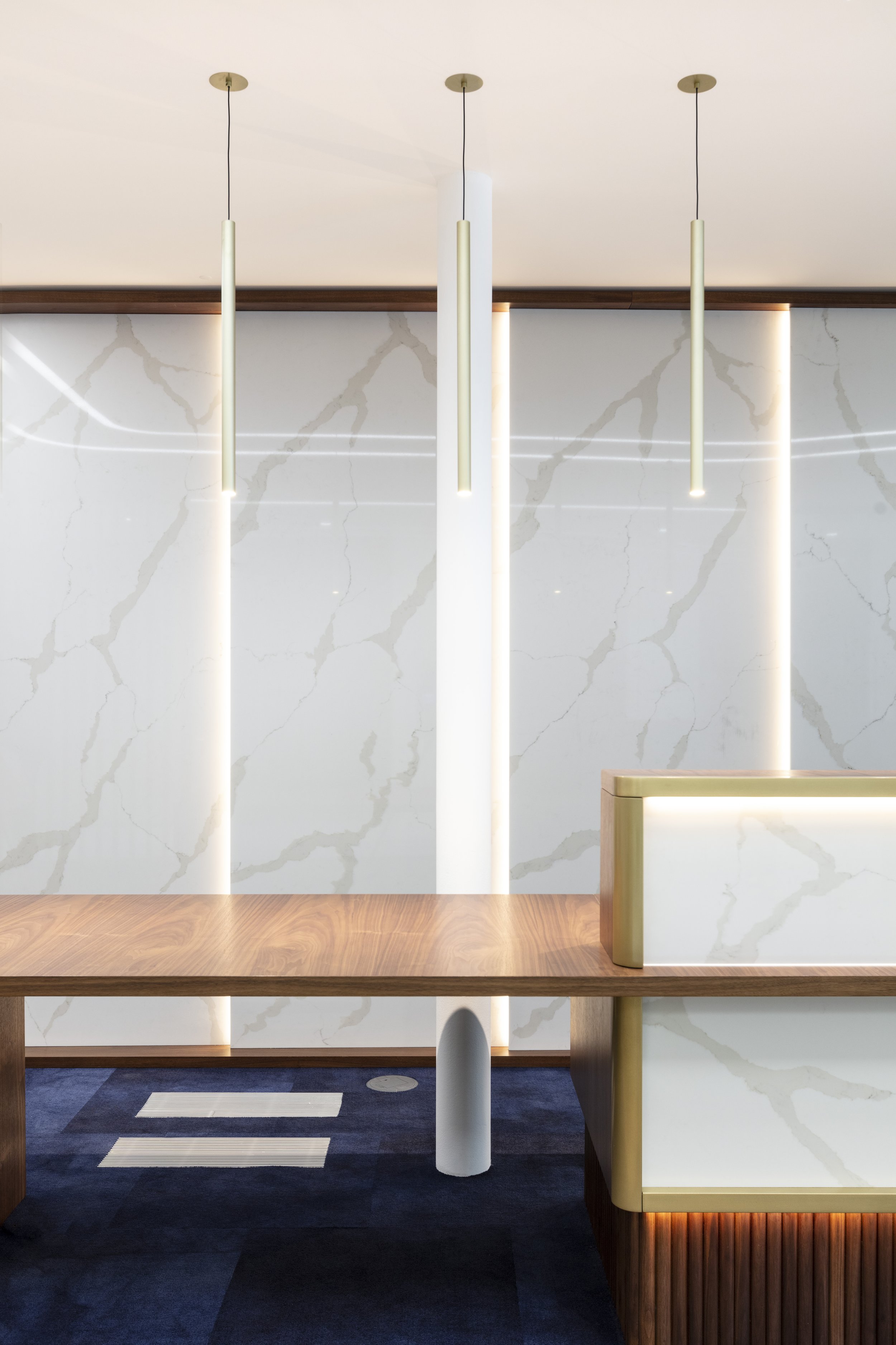 Modern lobby or reception area with a marble wall, wooden reception desk with gold accents, and hanging pendant lights.
