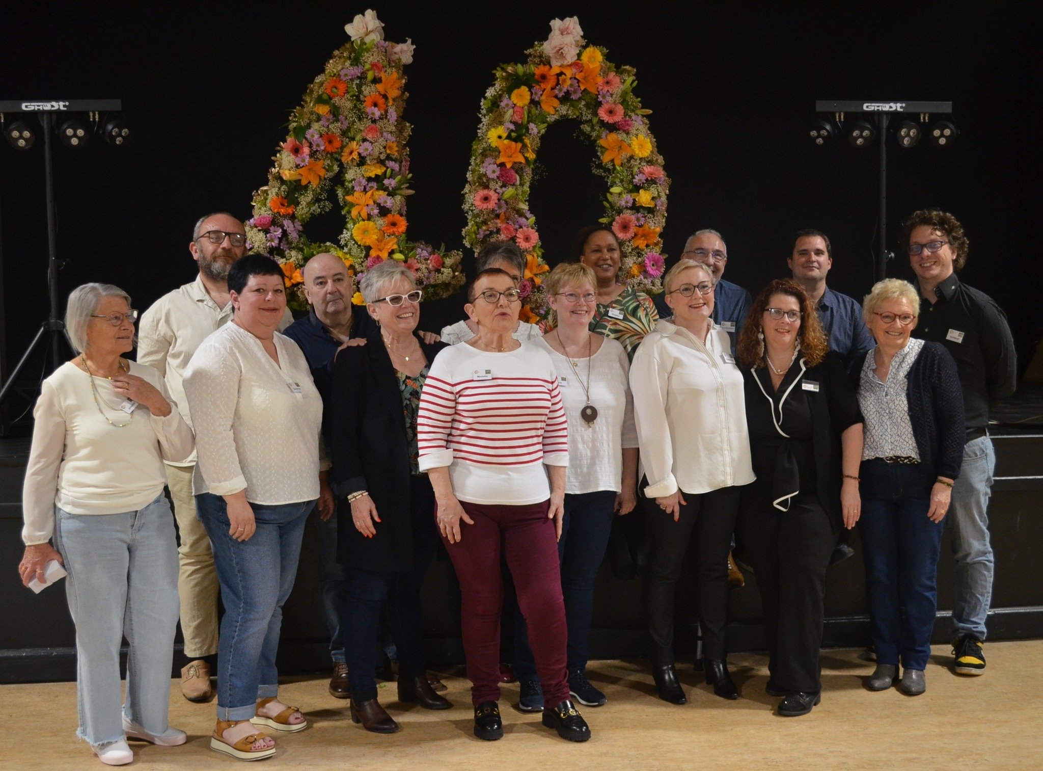 Groupe de personnes posant devant deux grands cœurs faits de fleurs, lors d'une cérémonie ou d'un événement