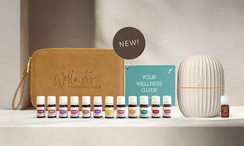 A collection of essential oils, a wellness guide, and a white ceramic diffuser on a white shelf, with a mustard-colored zippered pouch and a circular "New!" sign.