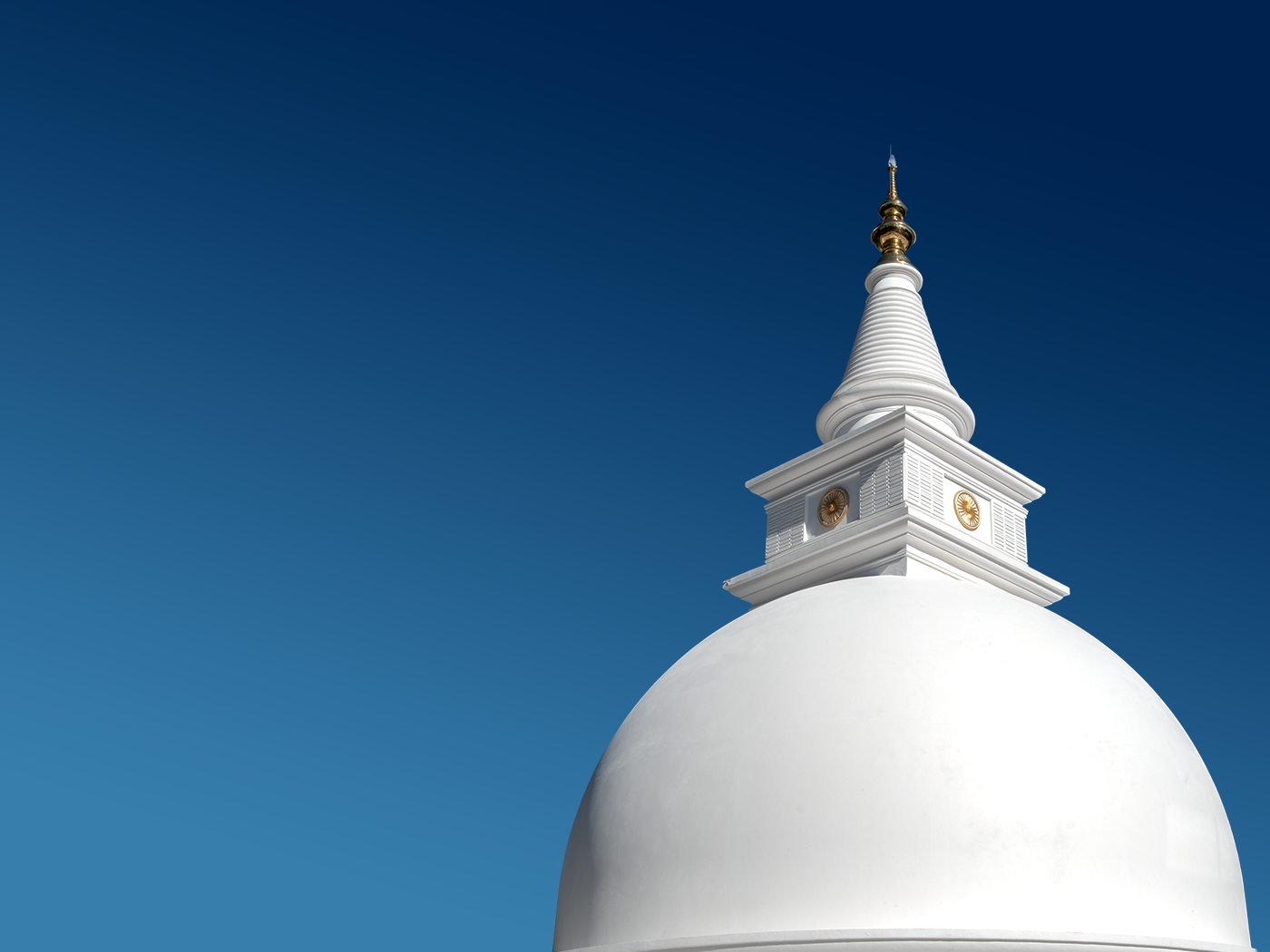 Close-up of a white Buddhist stupa with a golden spire against a clear blue sky.