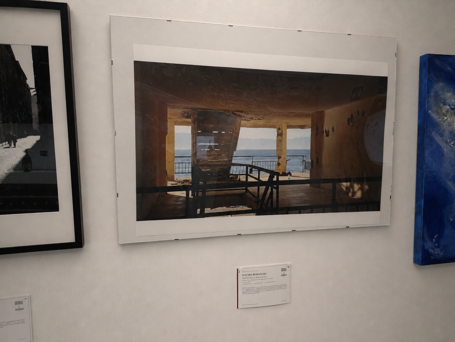 Una fotografia di un'opera d'arte che rappresenta un interno di una struttura in legno con vista sull'oceano, visibile attraverso le aperture.
