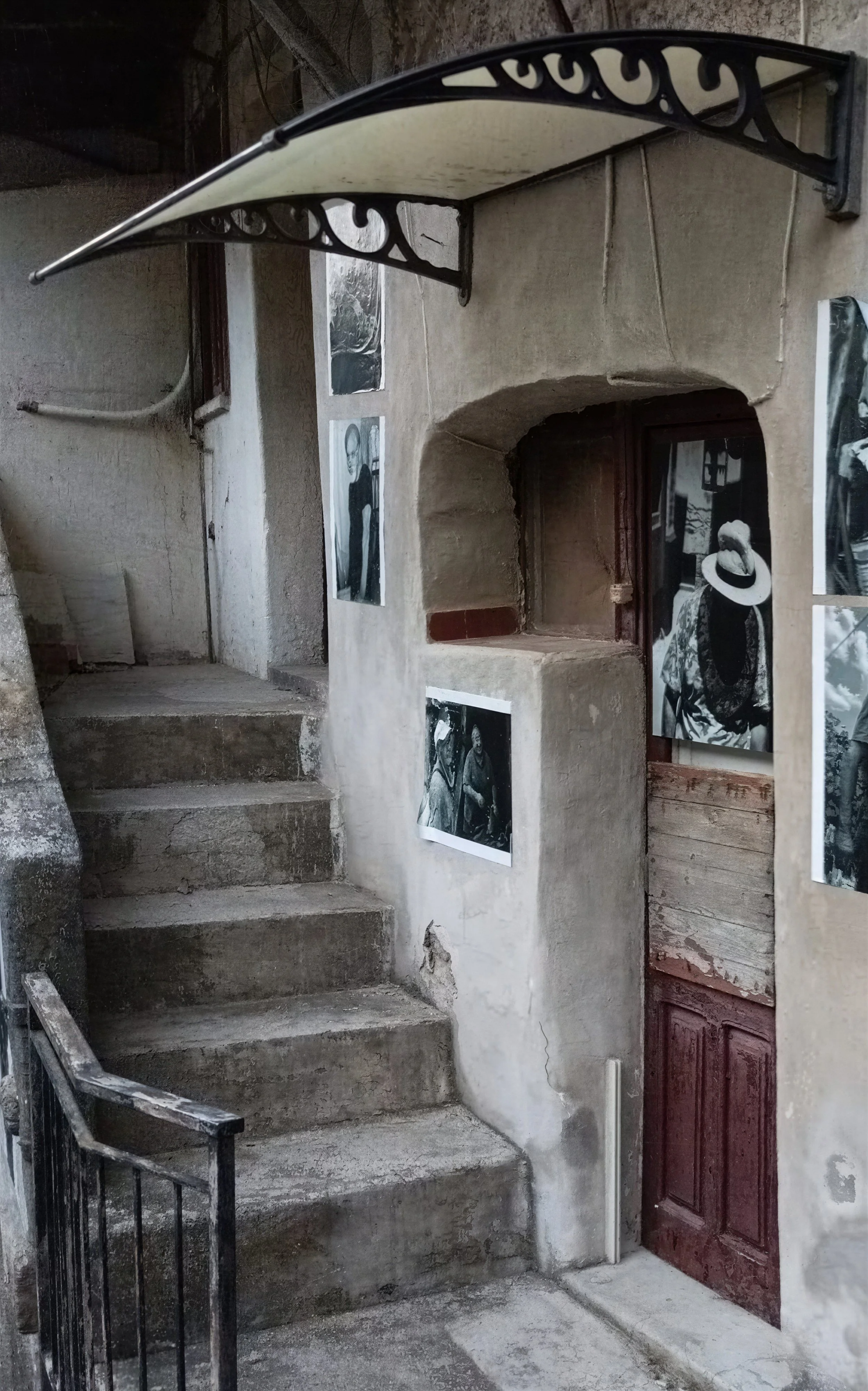 Scorci di una scala in pietra con pareti in gesso, decorata con fotografie in bianco e nero, e una porta in legno scuro.