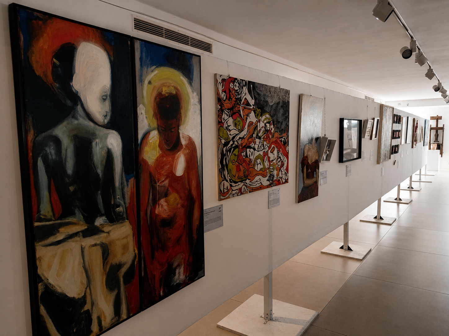 Mostra di dipinti e opere d'arte in una galleria, con pannelli espositivi affollati di quadri colorati e figure astratte.