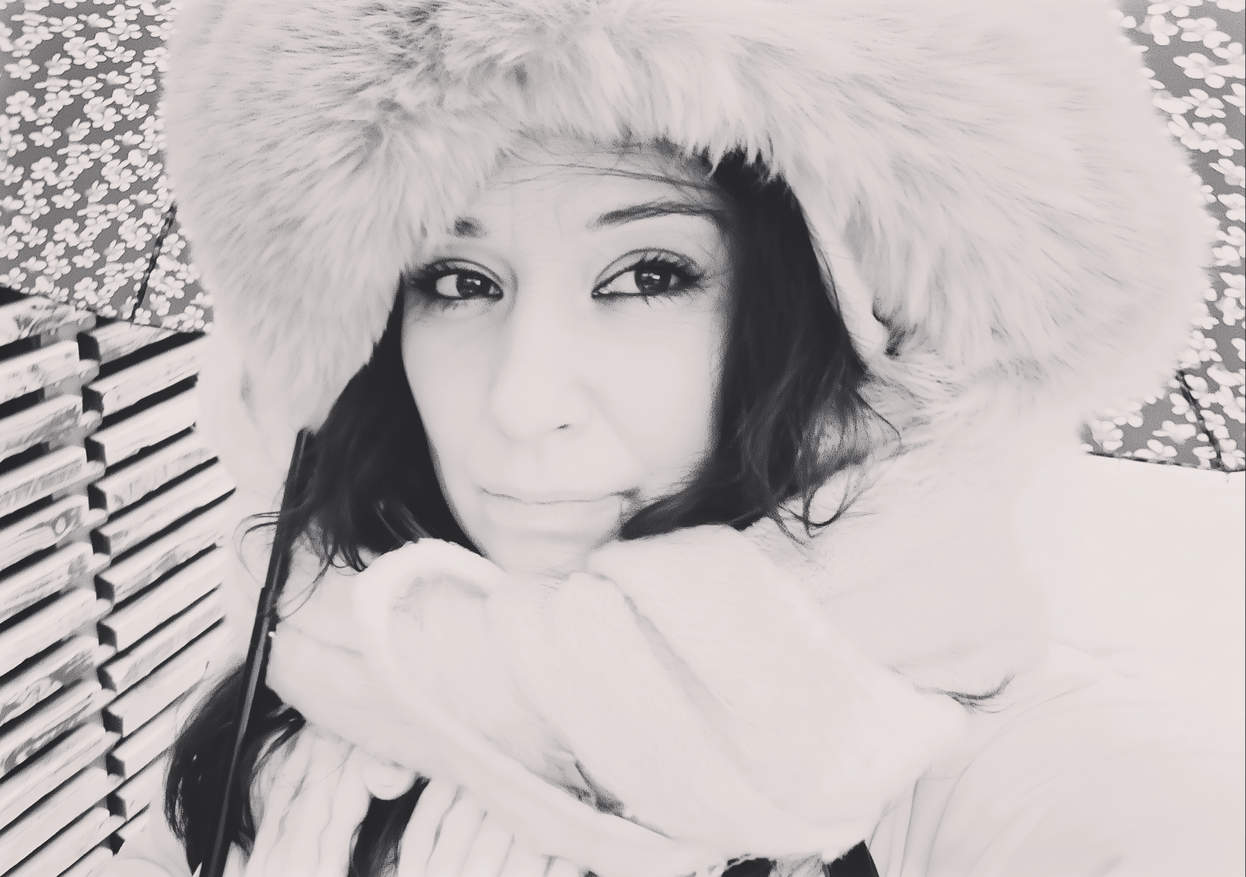 Un primo piano in bianco e nero di una donna con cappello di pelliccia e capigliatura lunga e scura, che sorride leggermente.