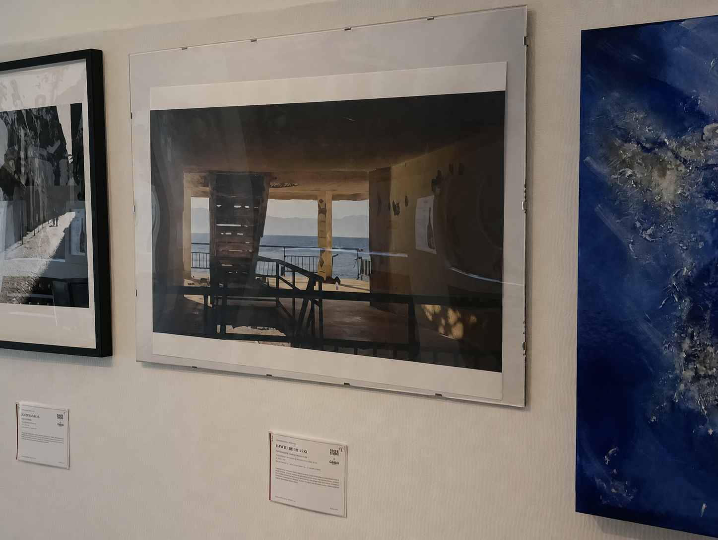 Fotografia di un'opera d'arte esposta in una mostra, raffigurante un interno di una struttura con vista sull'oceano.