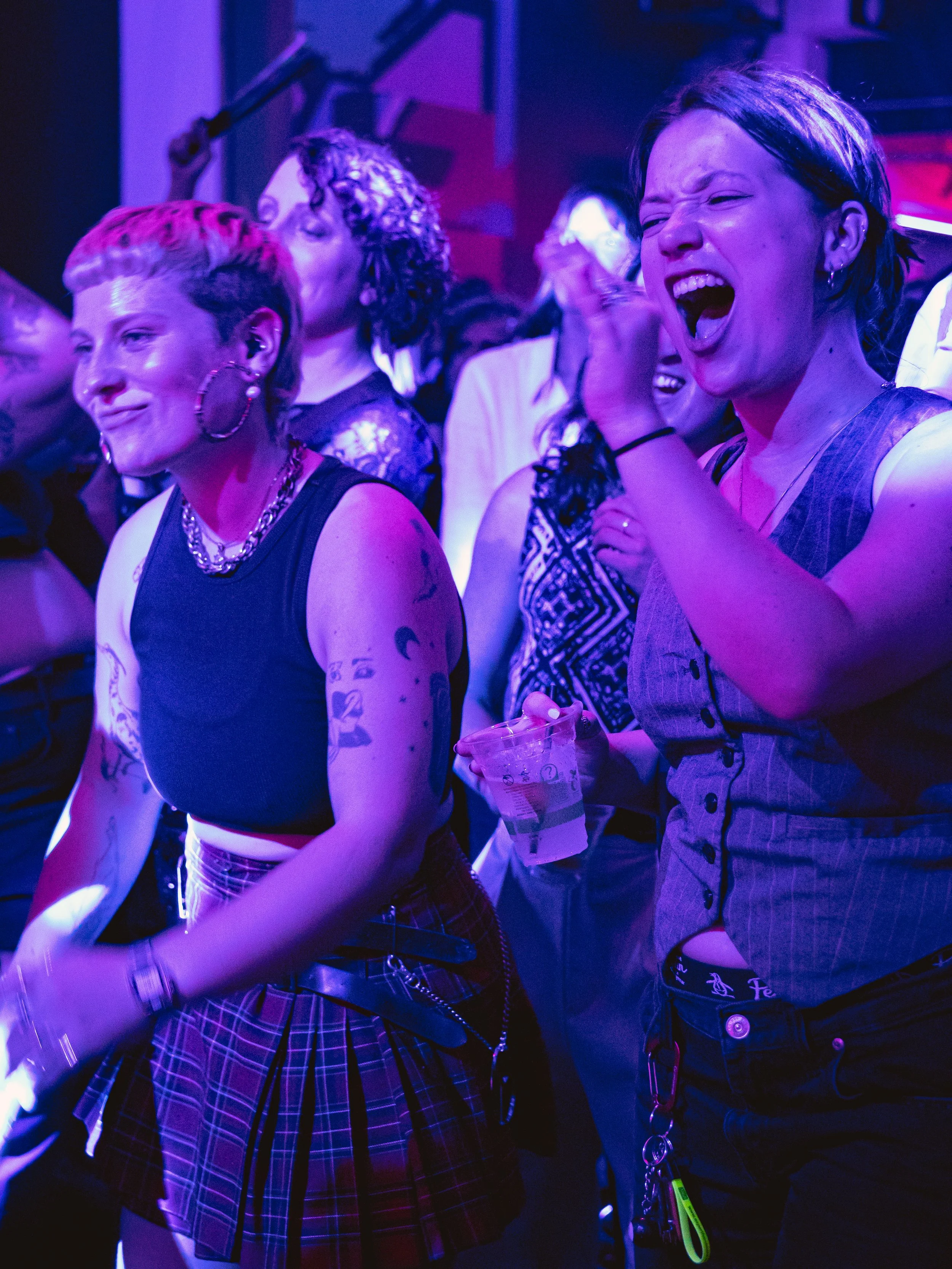 People at a lively event or concert enjoying and reacting vocally, with colorful purple and blue lighting creating an energetic atmosphere.