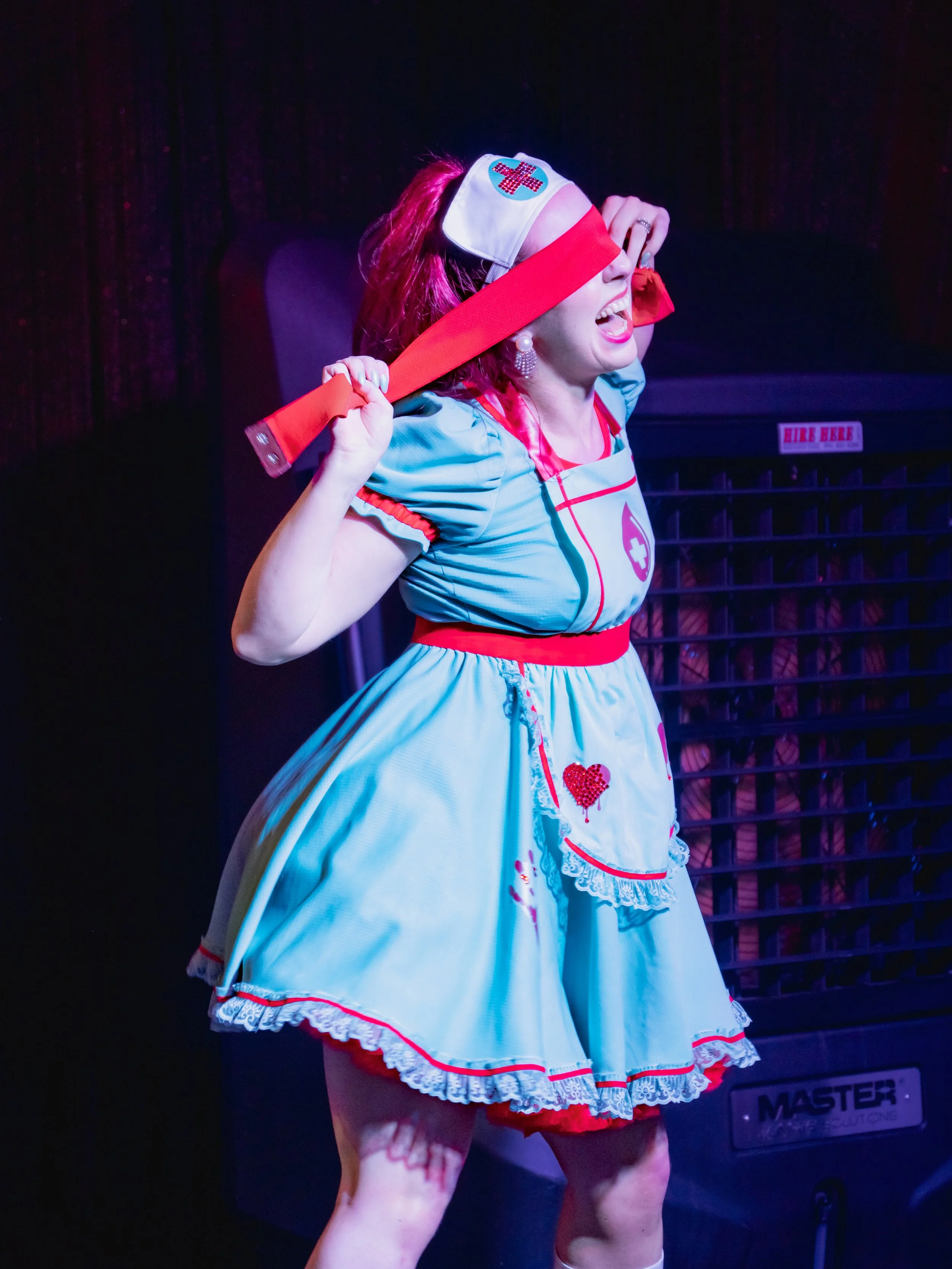 Performer dressed as a nurse holding a large red prop glove on stage.