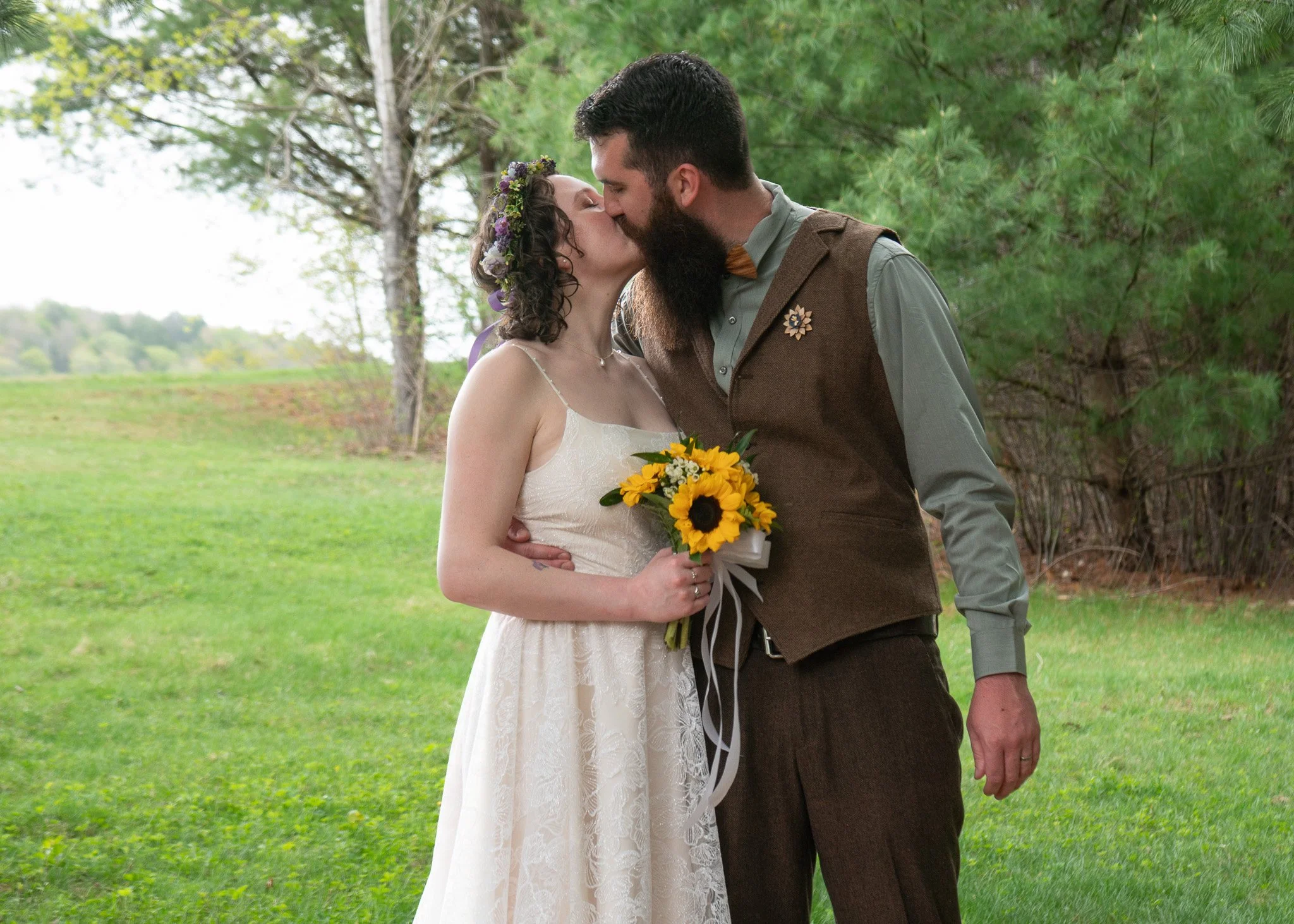 A newlywed couple is kissing while the bride holds her bouquet