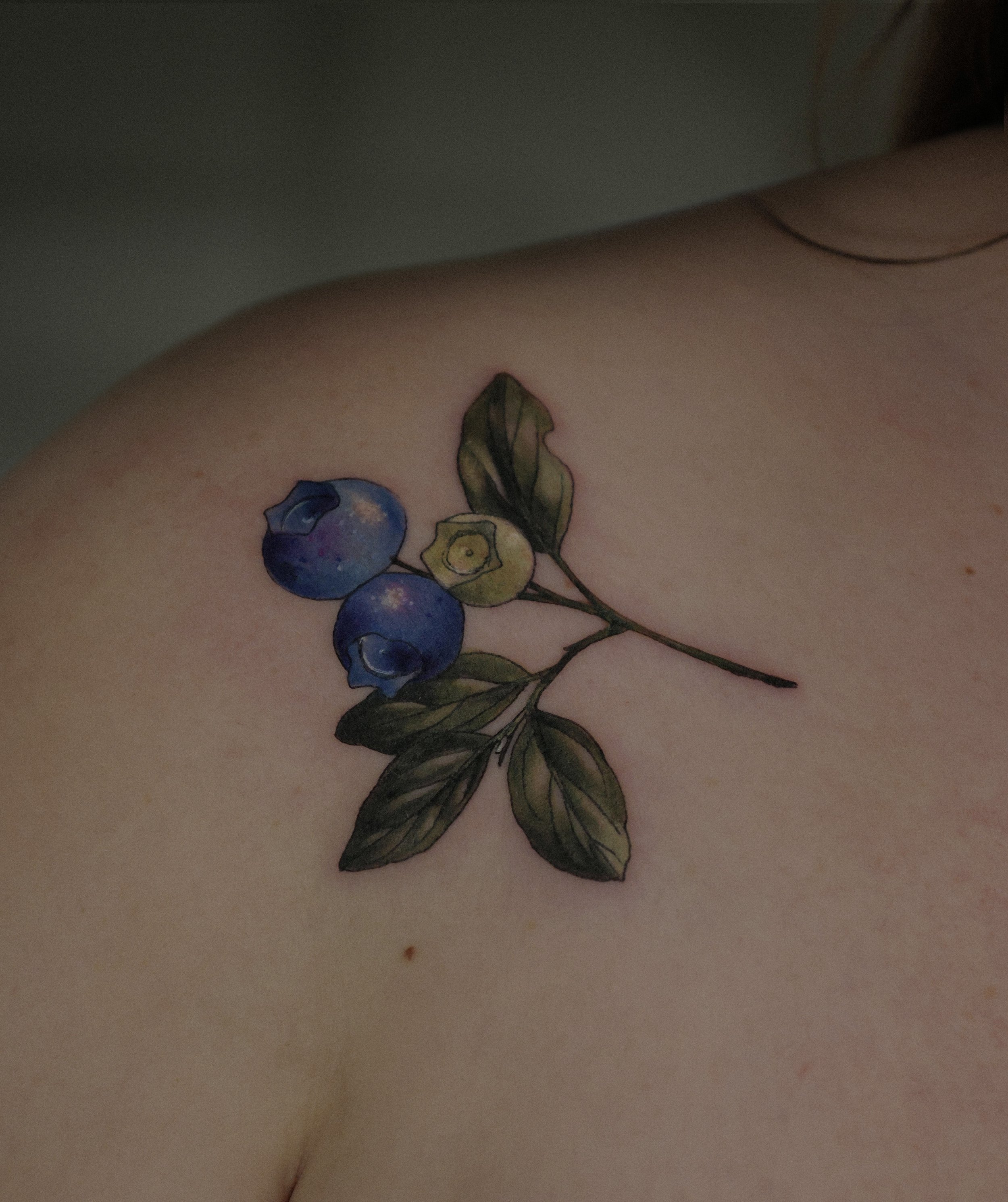 Farbiges feines Tattoo auf einer Frau, das einen Zweig aus Blaubeeren zeigt