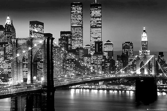 Black and white photo of the New York City skyline at night, featuring the Brooklyn Bridge in the foreground and skyscrapers including the Twin Towers and Empire State Building in the background.
